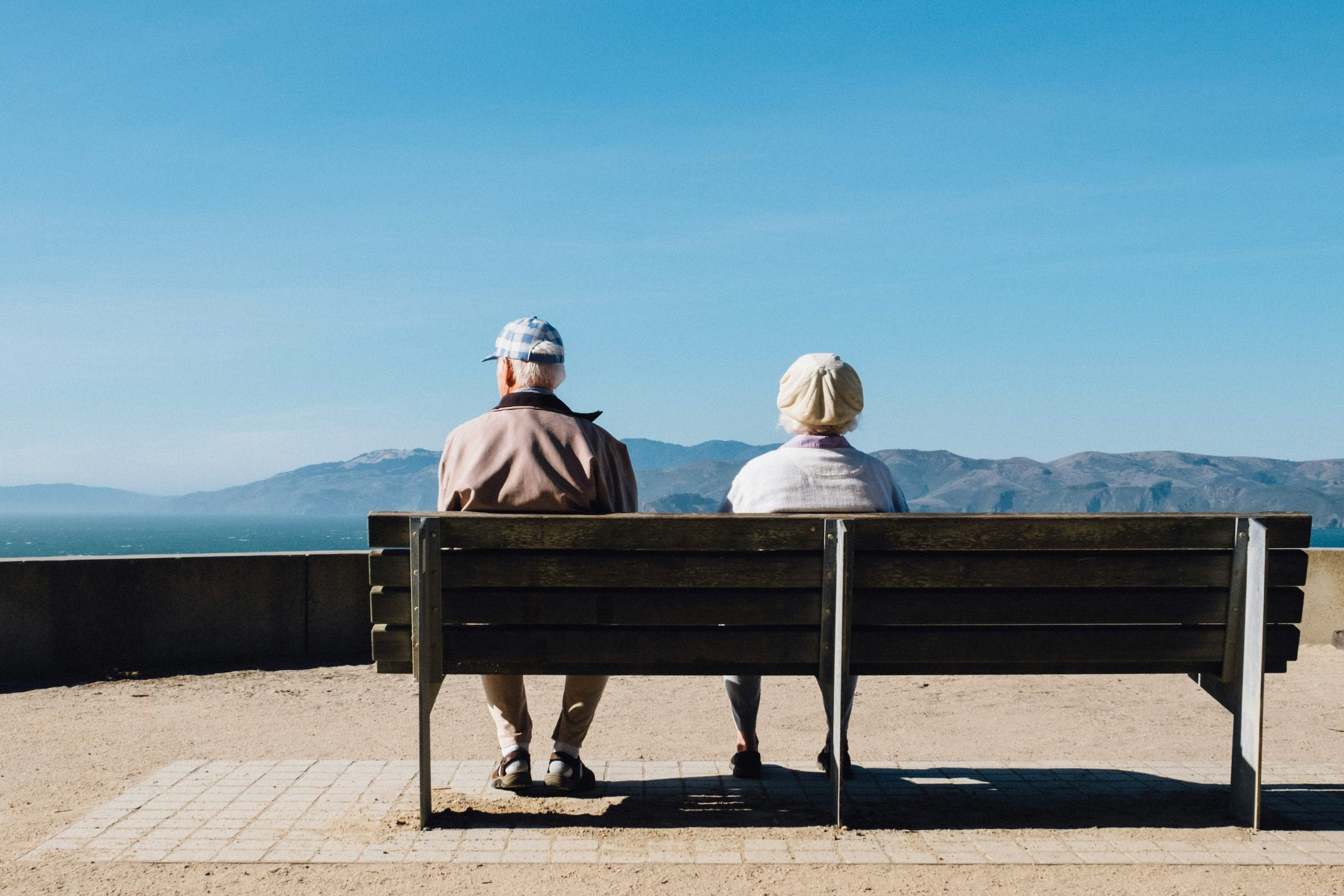 Elderly couple sitting on a bench looking out by Matt Bennett.