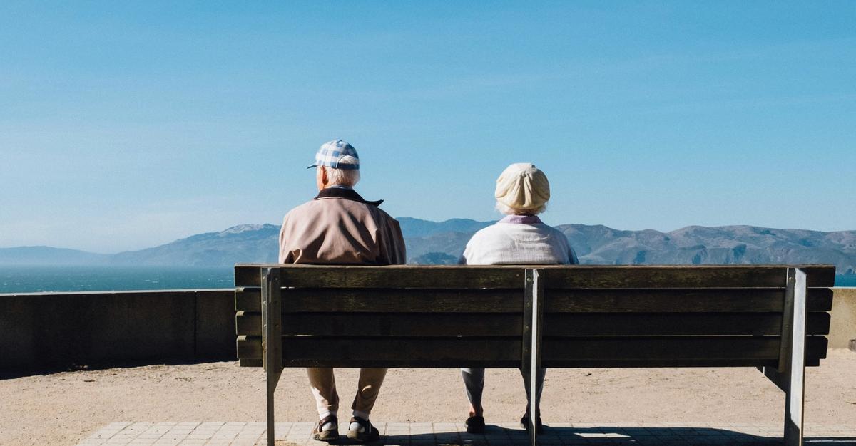 Elderly couple sitting on a bench looking out by Matt Bennett.