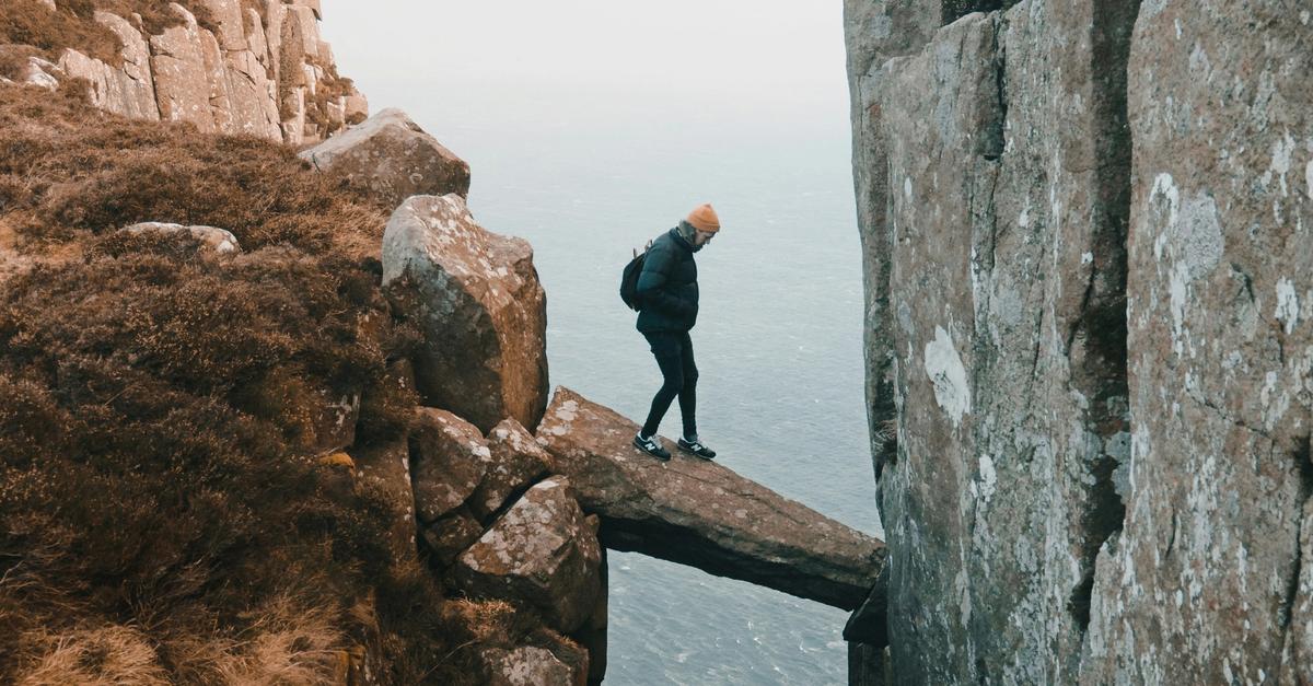Man walking on a boulder in between two high peaks.