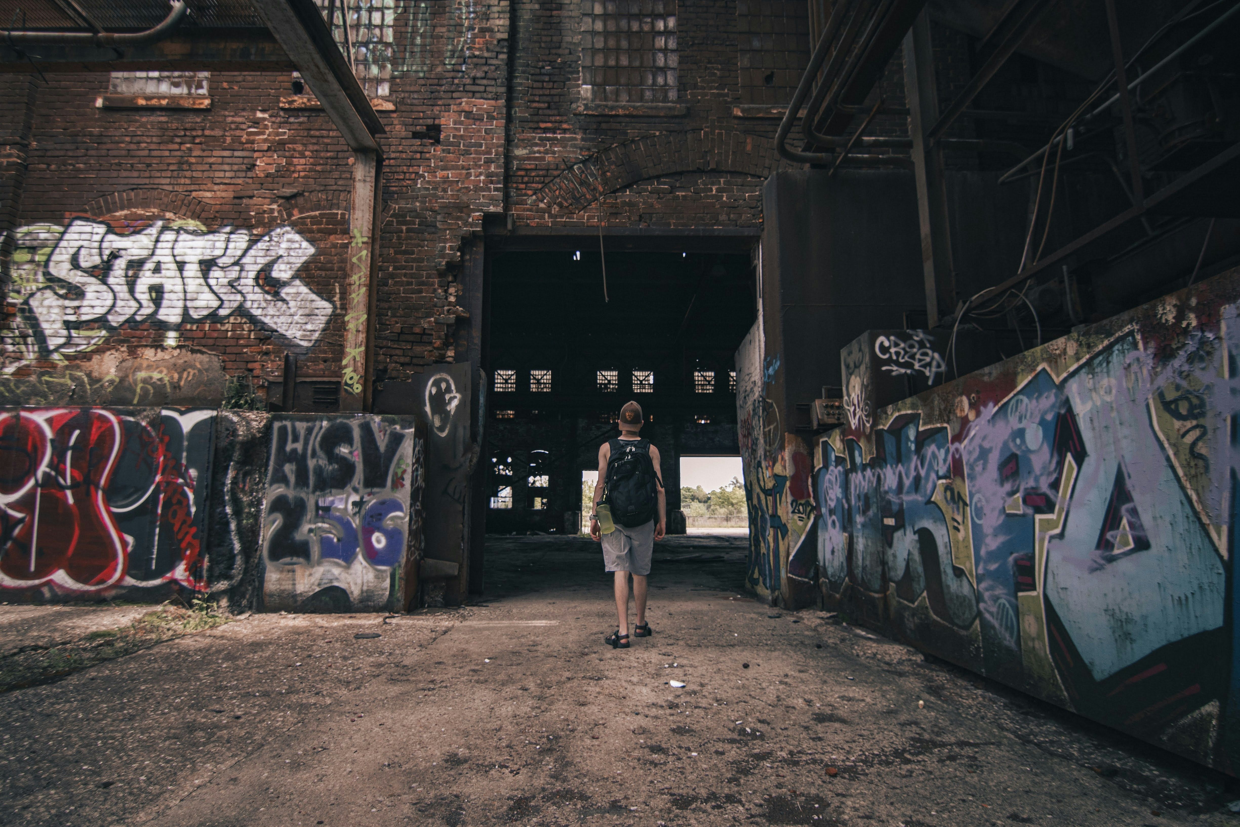 Man with back pack walking into an abandoned factor with graffiti. 