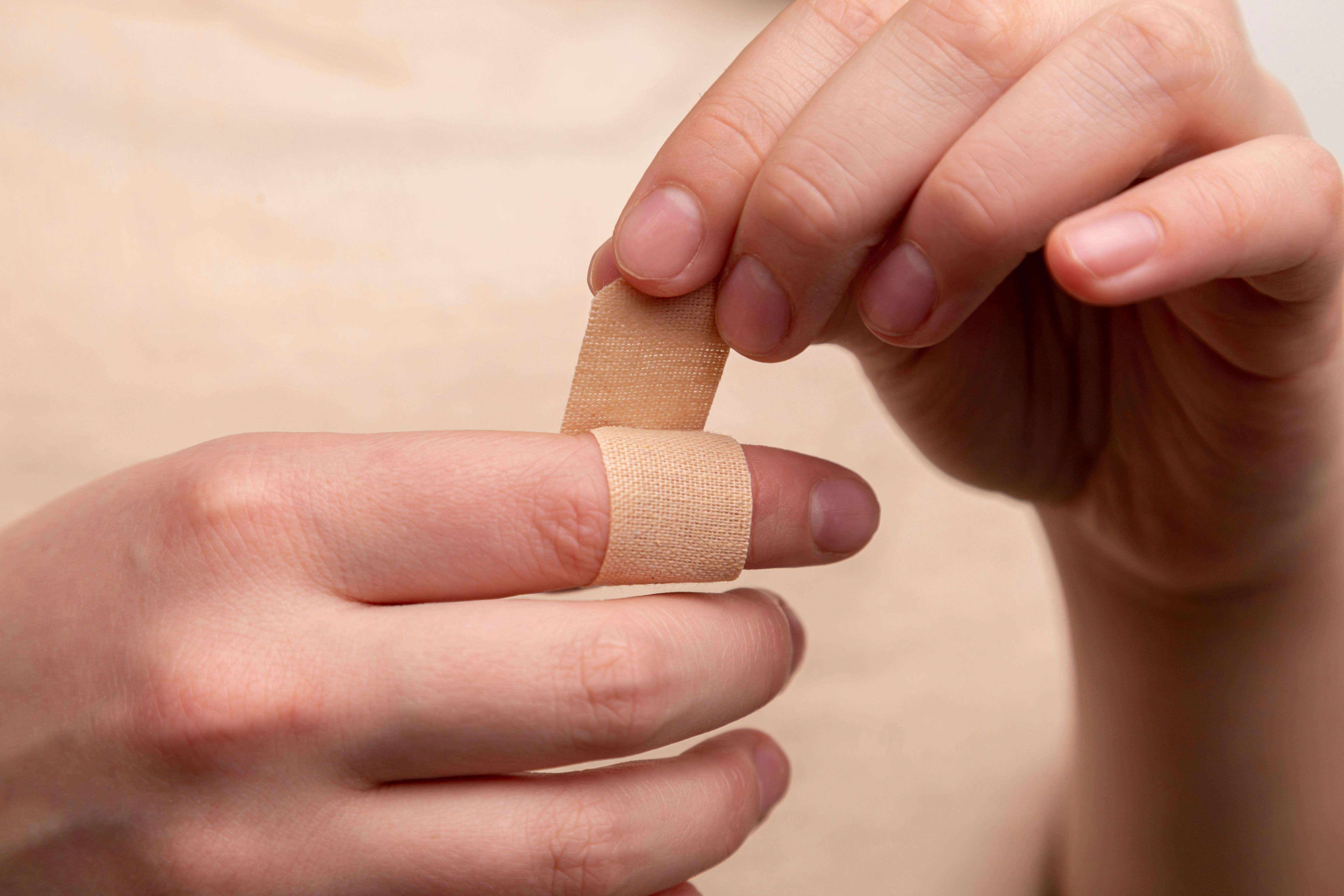 Image of individual wrapping there finger with a bandaid. 