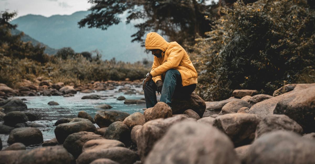 Man looking down at a river creek with rocks.