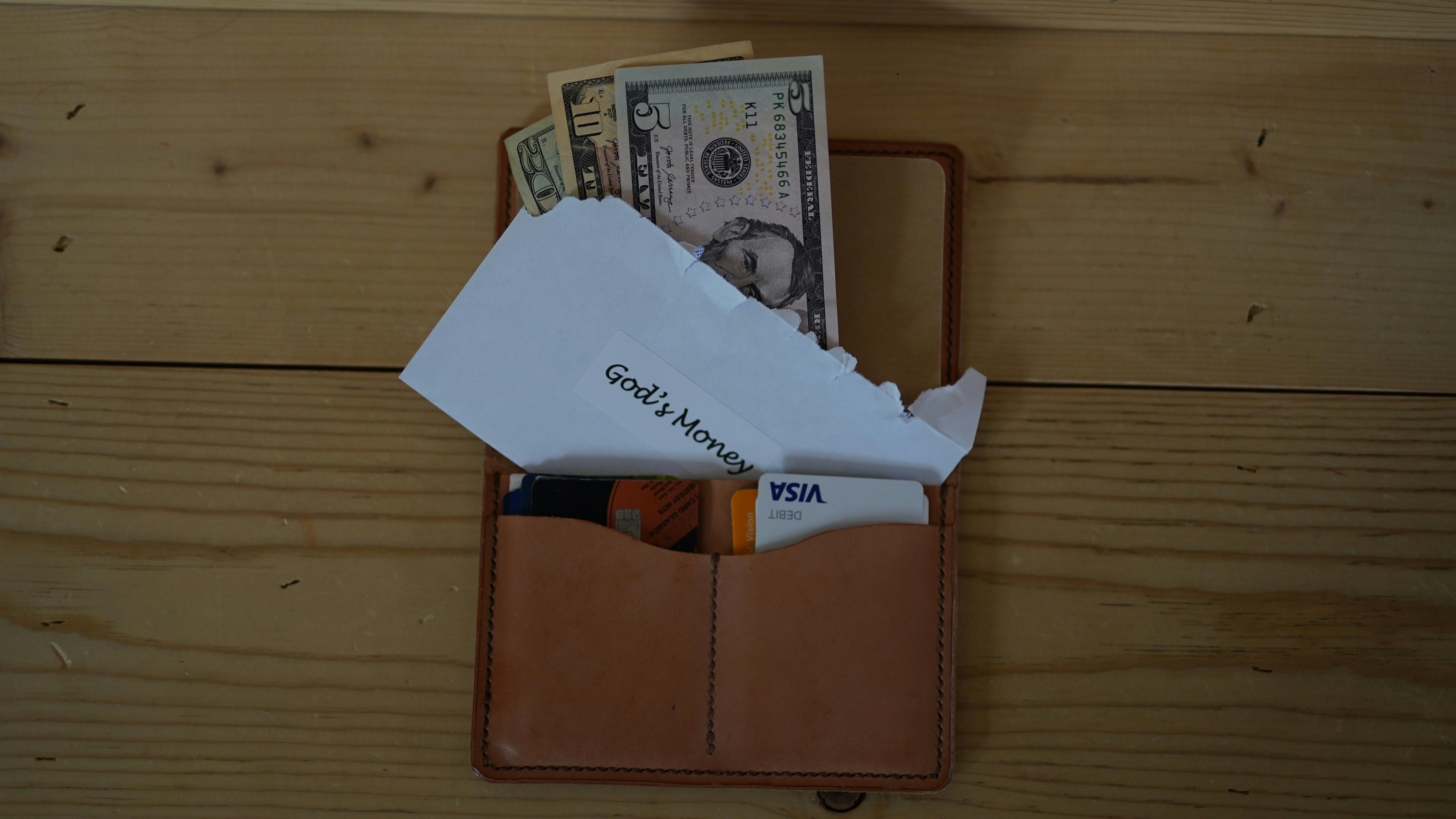 Wallet full of money on a desk with an envelope saying "God's money" on it.