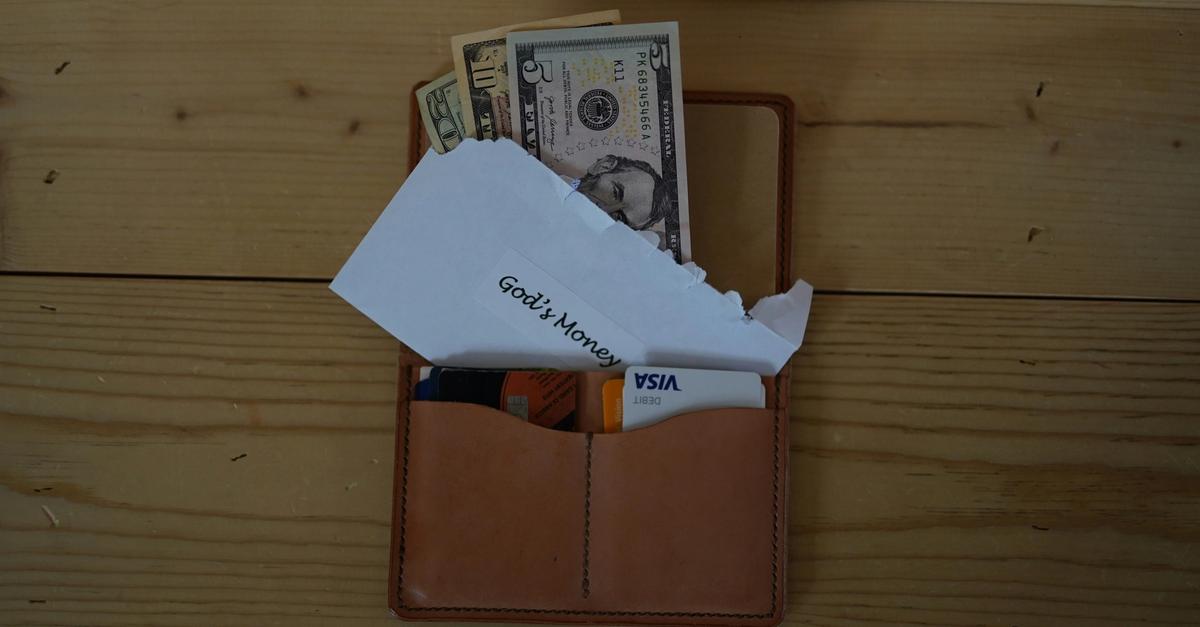 Wallet full of money on a desk with an envelope saying "God's money" on it.