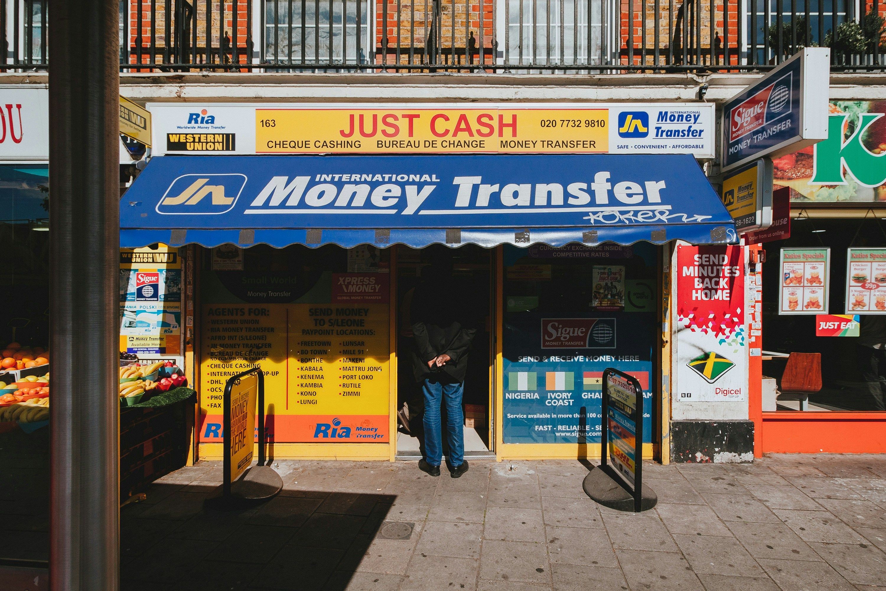 Storefront with sign saying Just Cash International Money Transfer by Alistair Macrobert.