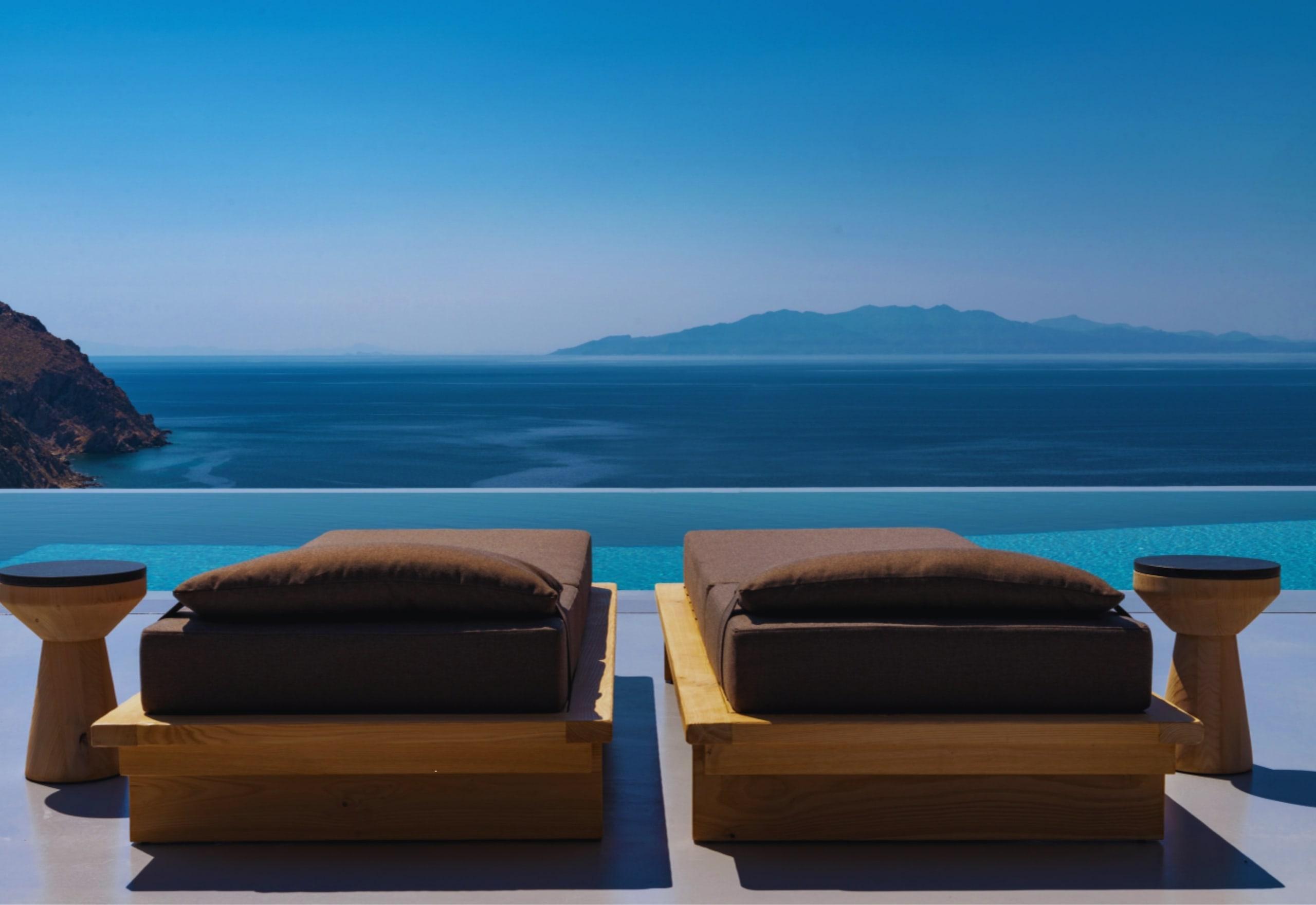 Two daybeds at the edge of a pool facing the Aegean