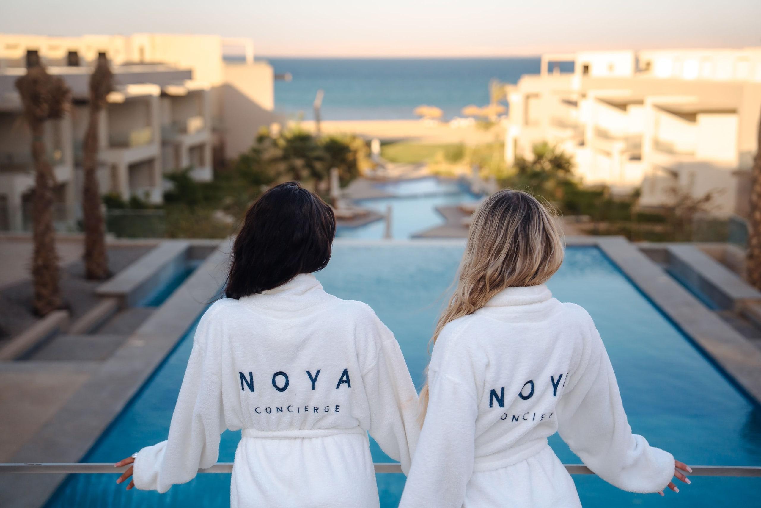 Two guests in NOYA robes on a terrace above a pool