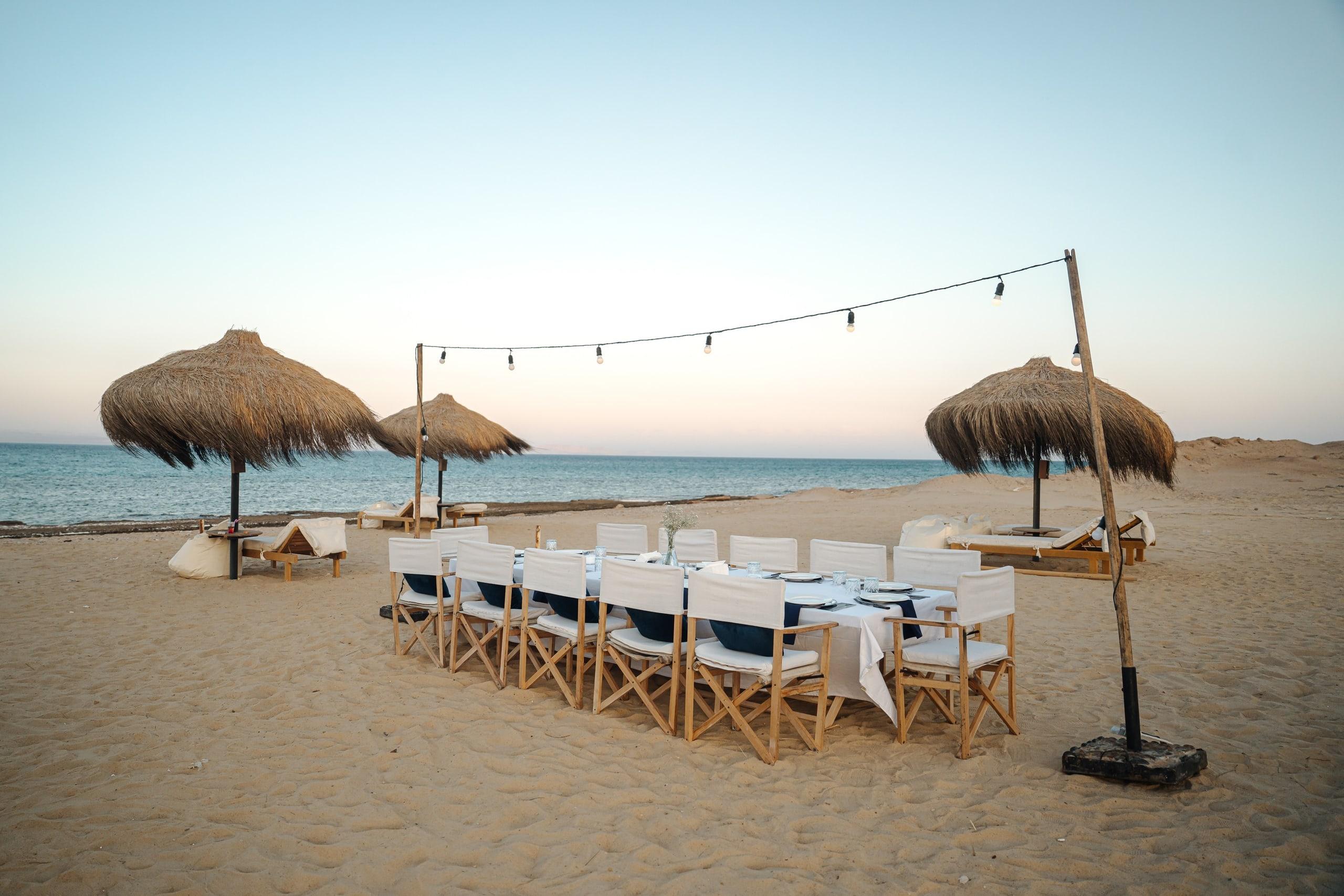 A long dinner table on the beach under string lights