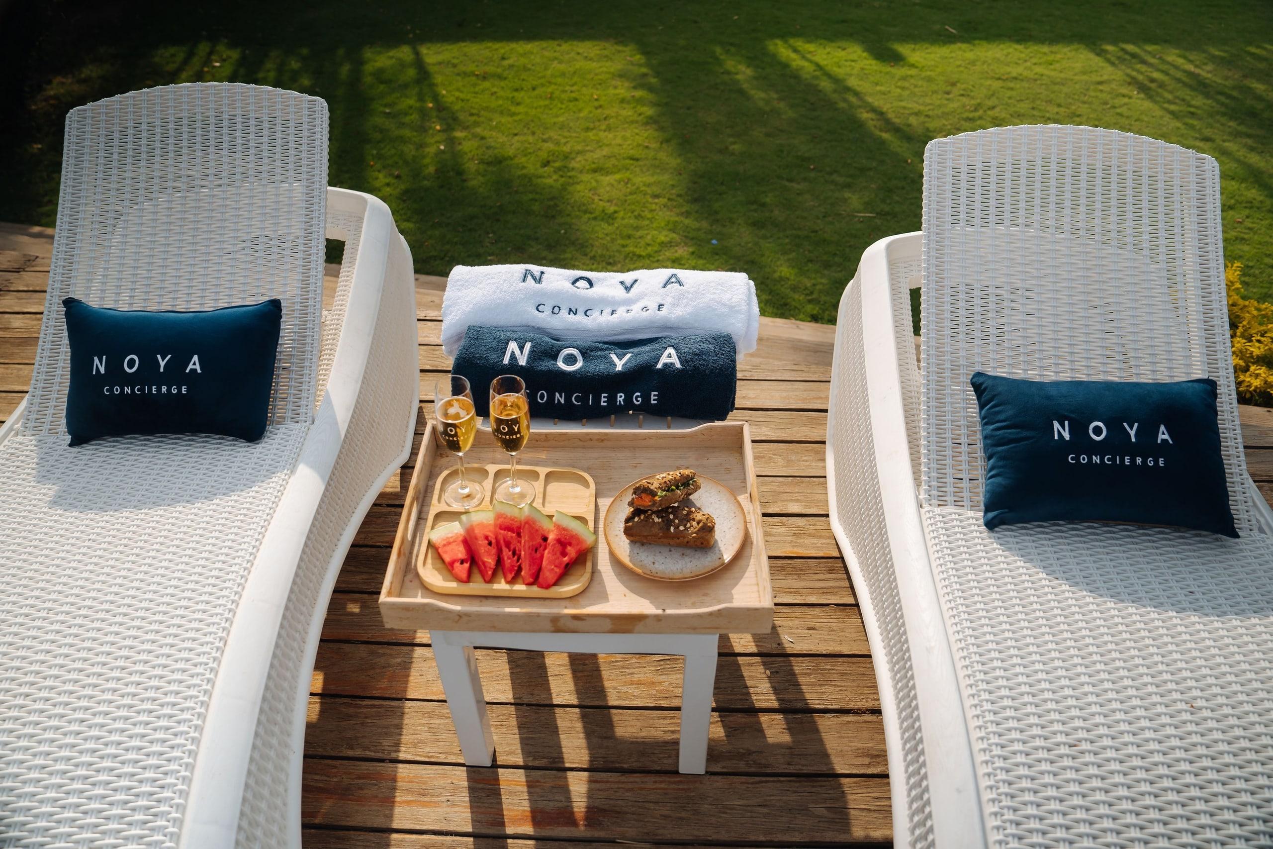 A NOYA table set between two poolside loungers