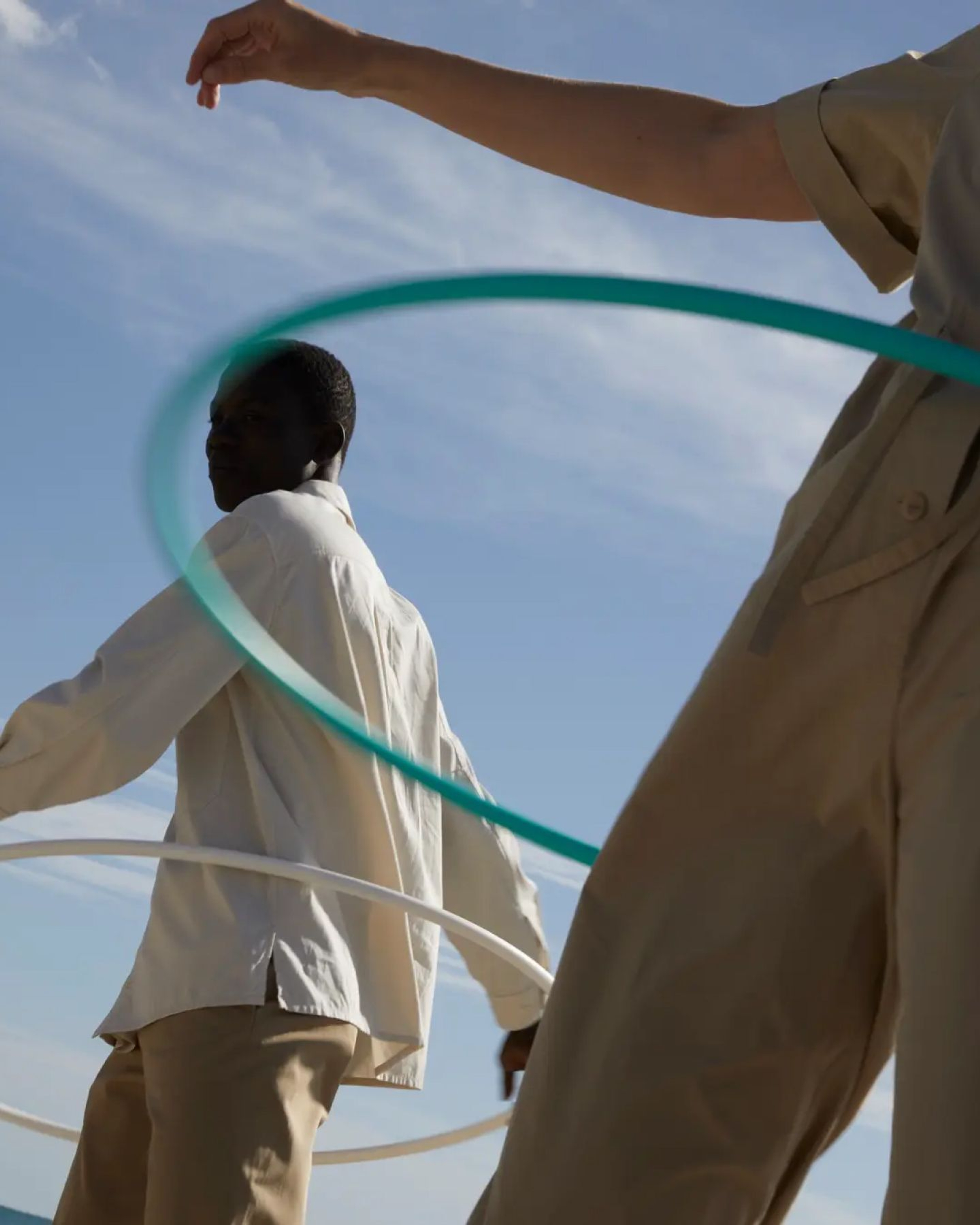 Two people in white shirts and khakis hula-hooping against a blue sky.