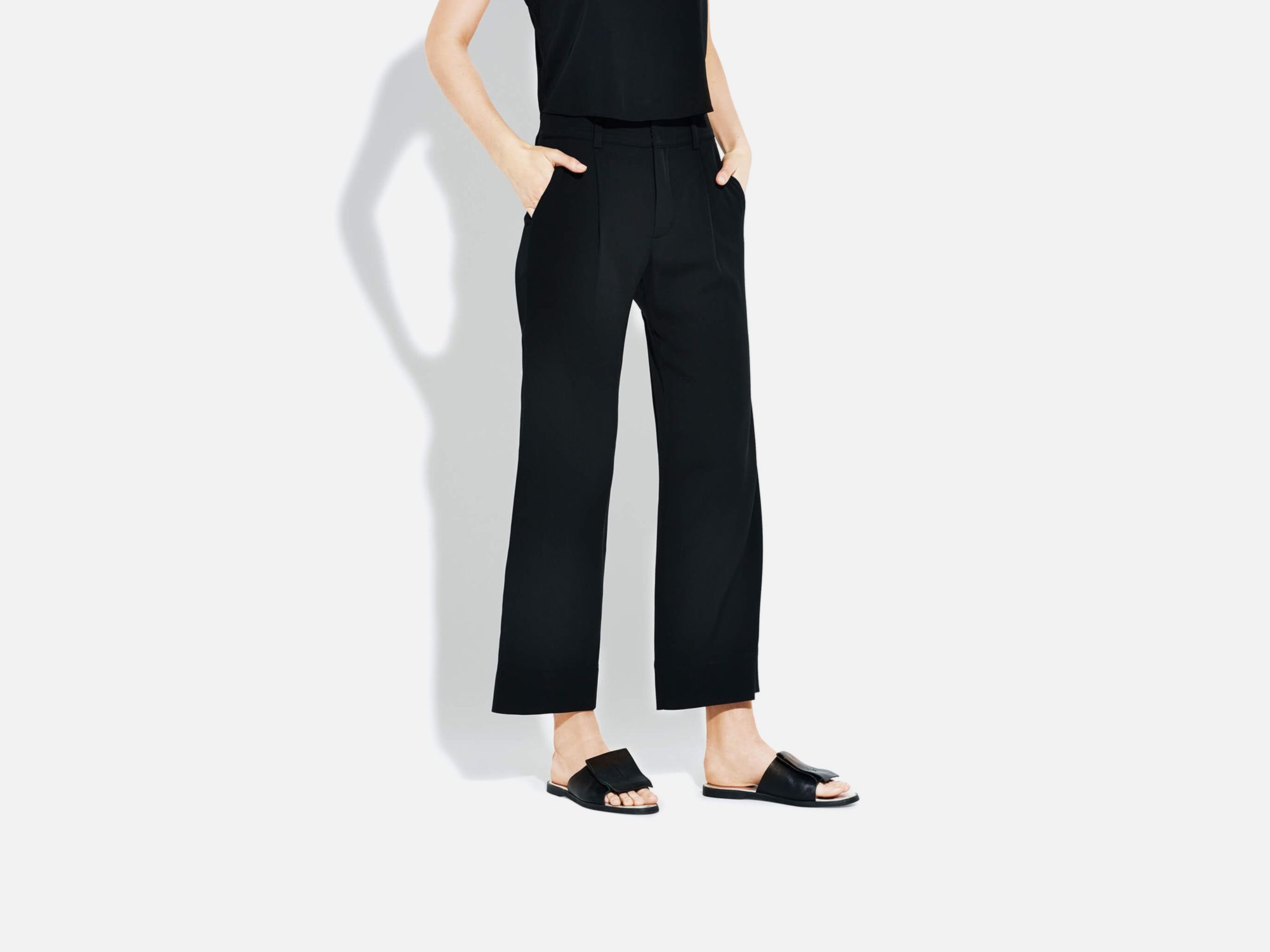 Bottom half of woman wearing black clothing with hands in pocket in front of light gray background