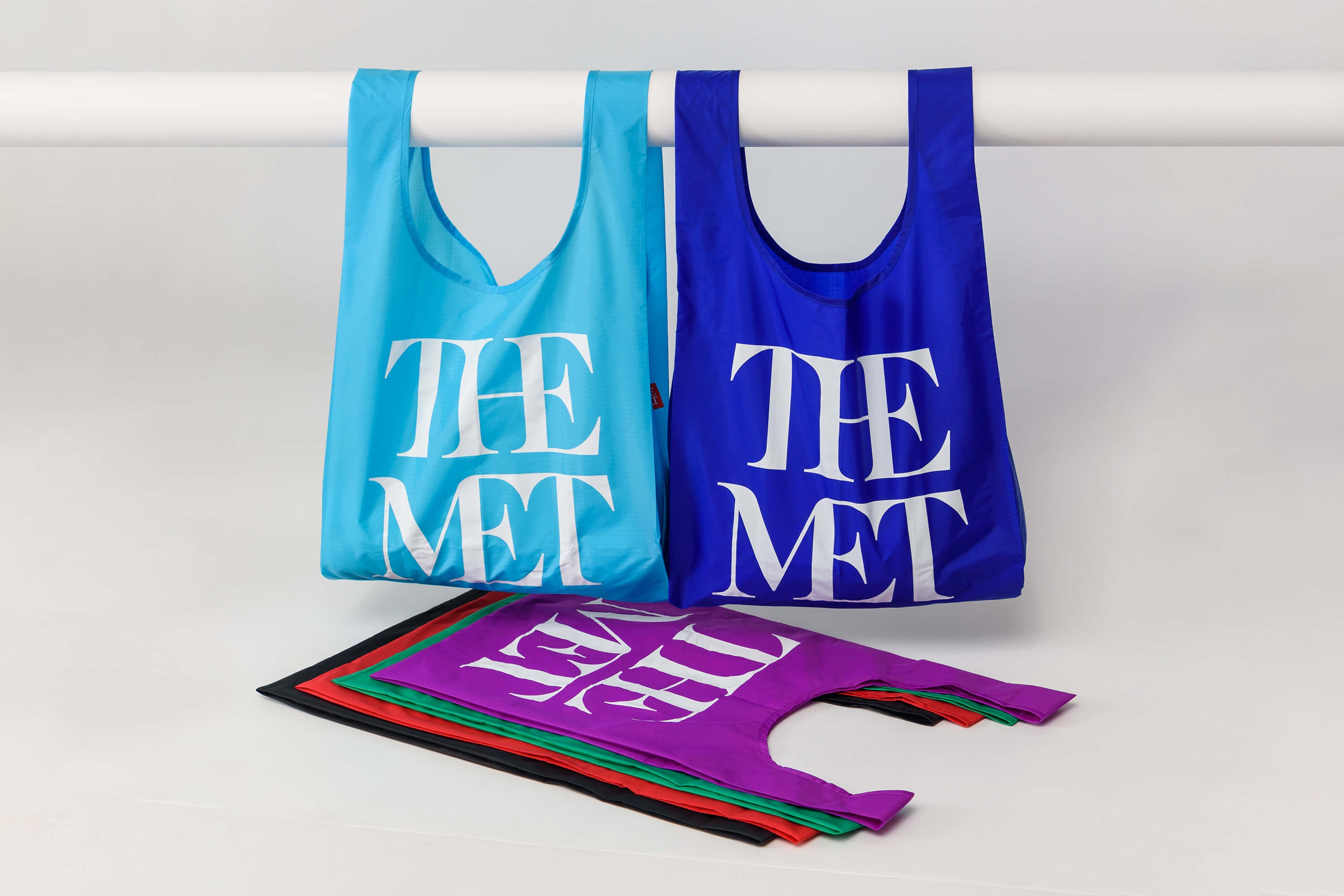 Two Baggu bags hanging on a stick with several bags flat underneath