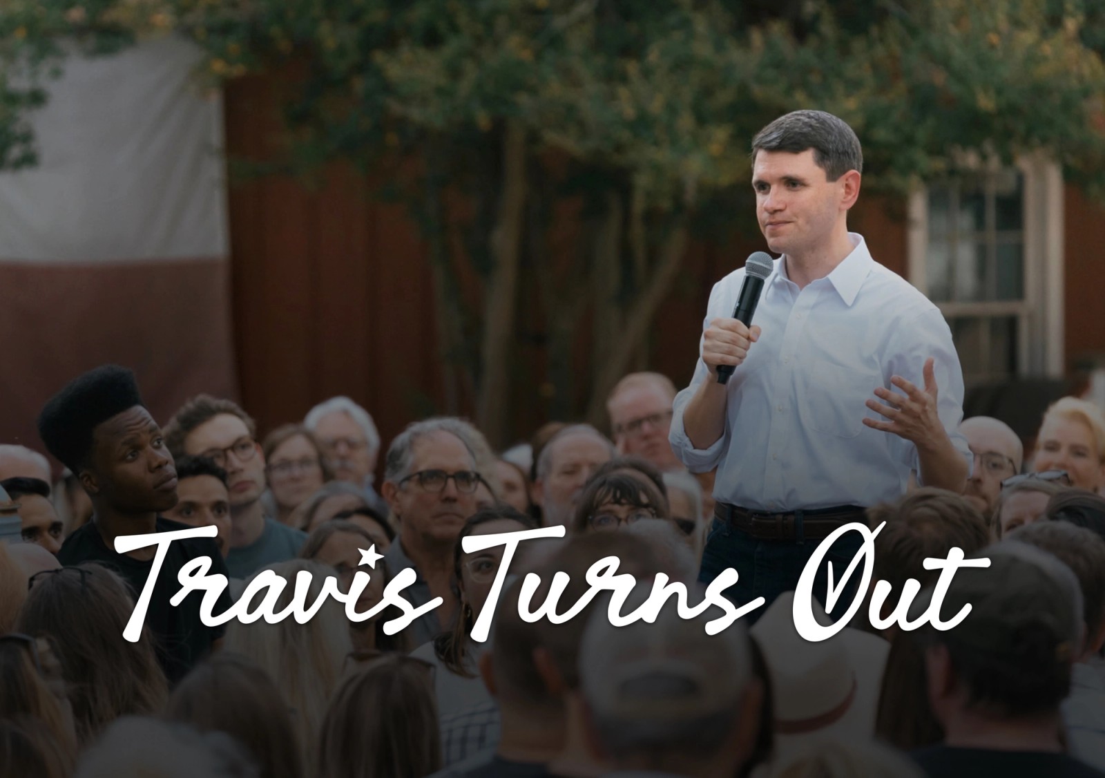 A candidate speaking to a crowd behind the Travis Turns Out wordmark