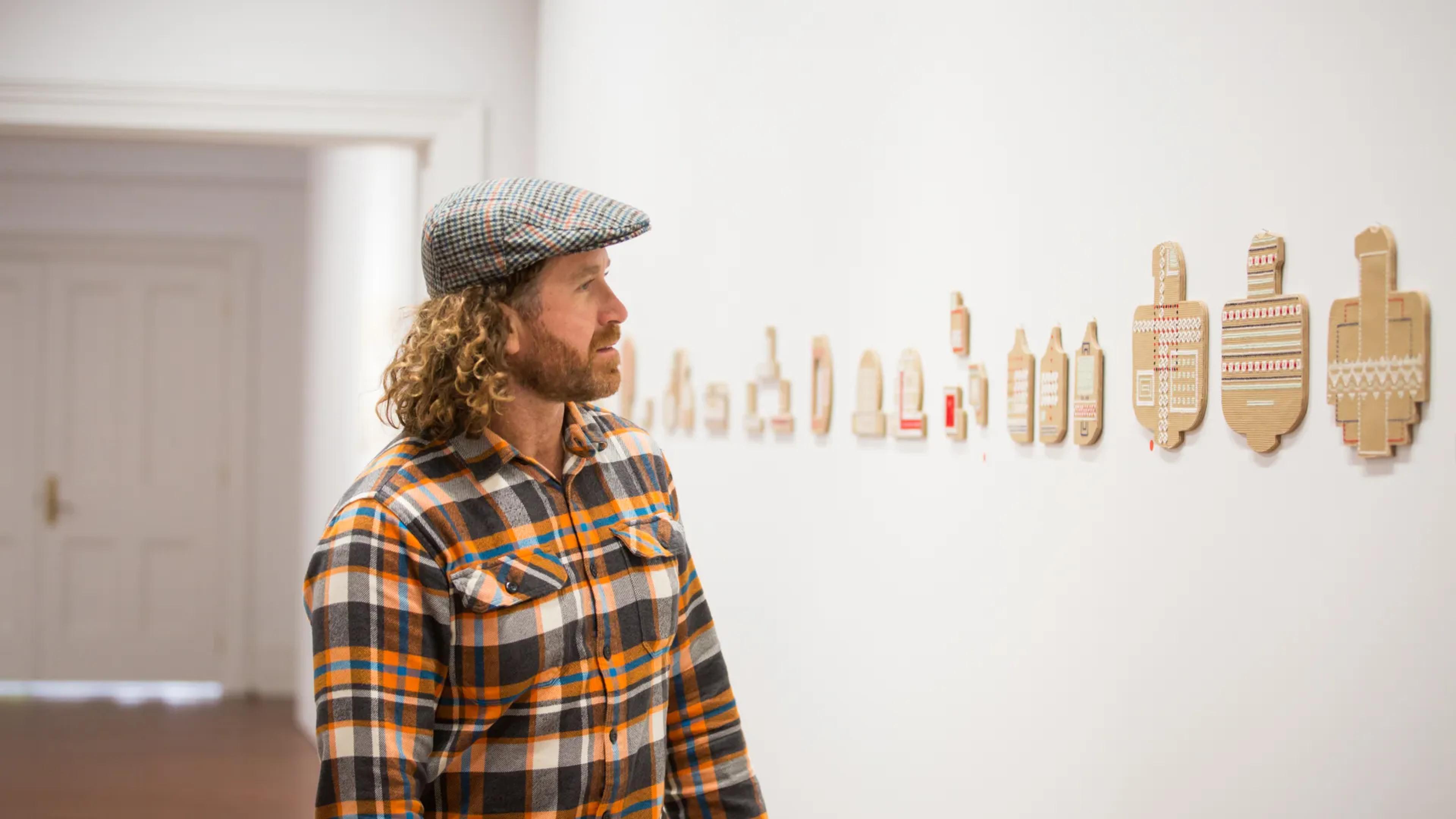 A photo of a man looking at some art on a wall.
