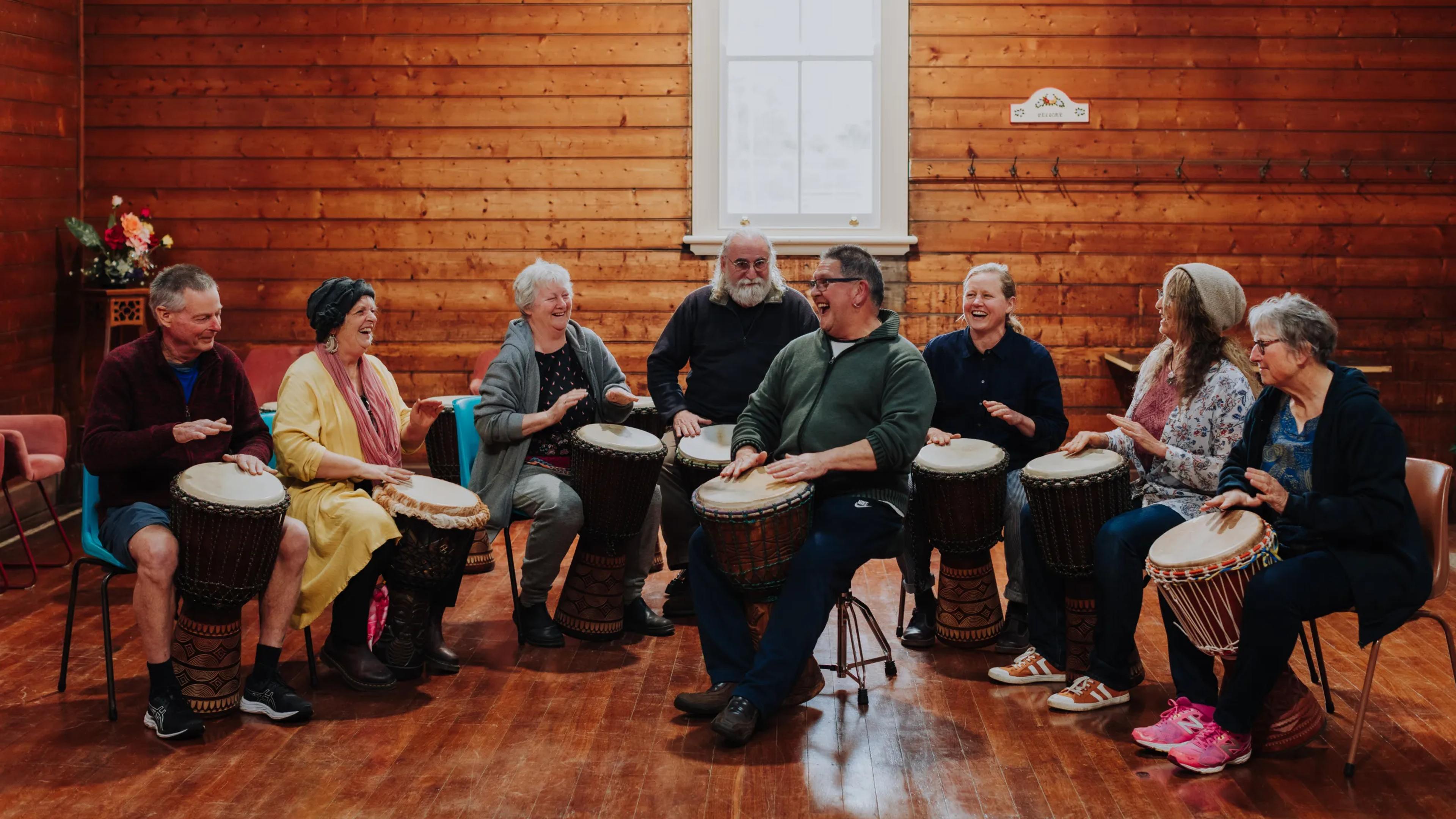 A photo of a group of people sitting on chairs with bongos, playing music.