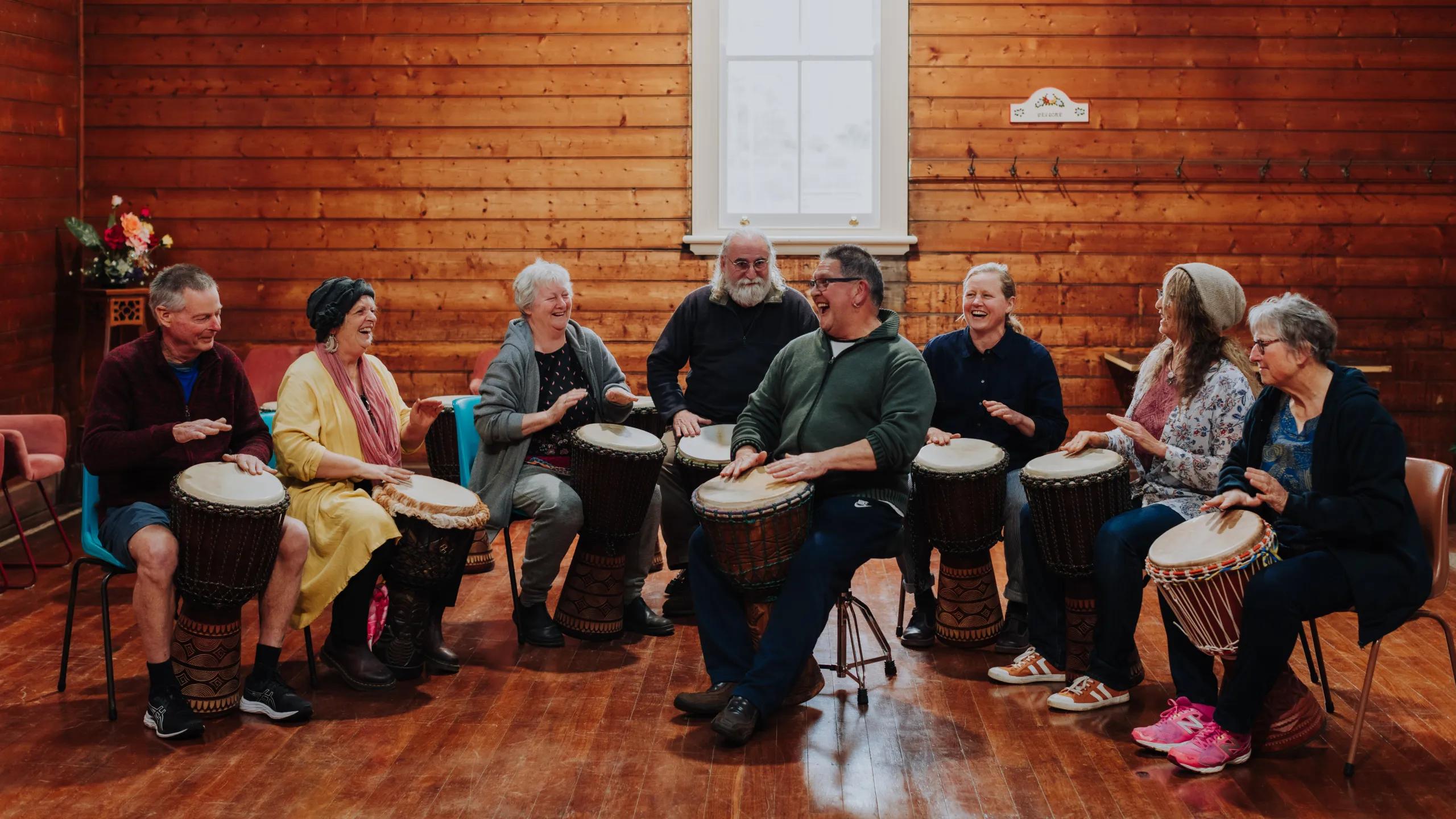 A photo of a group of people sitting on chairs with bongos, playing music.