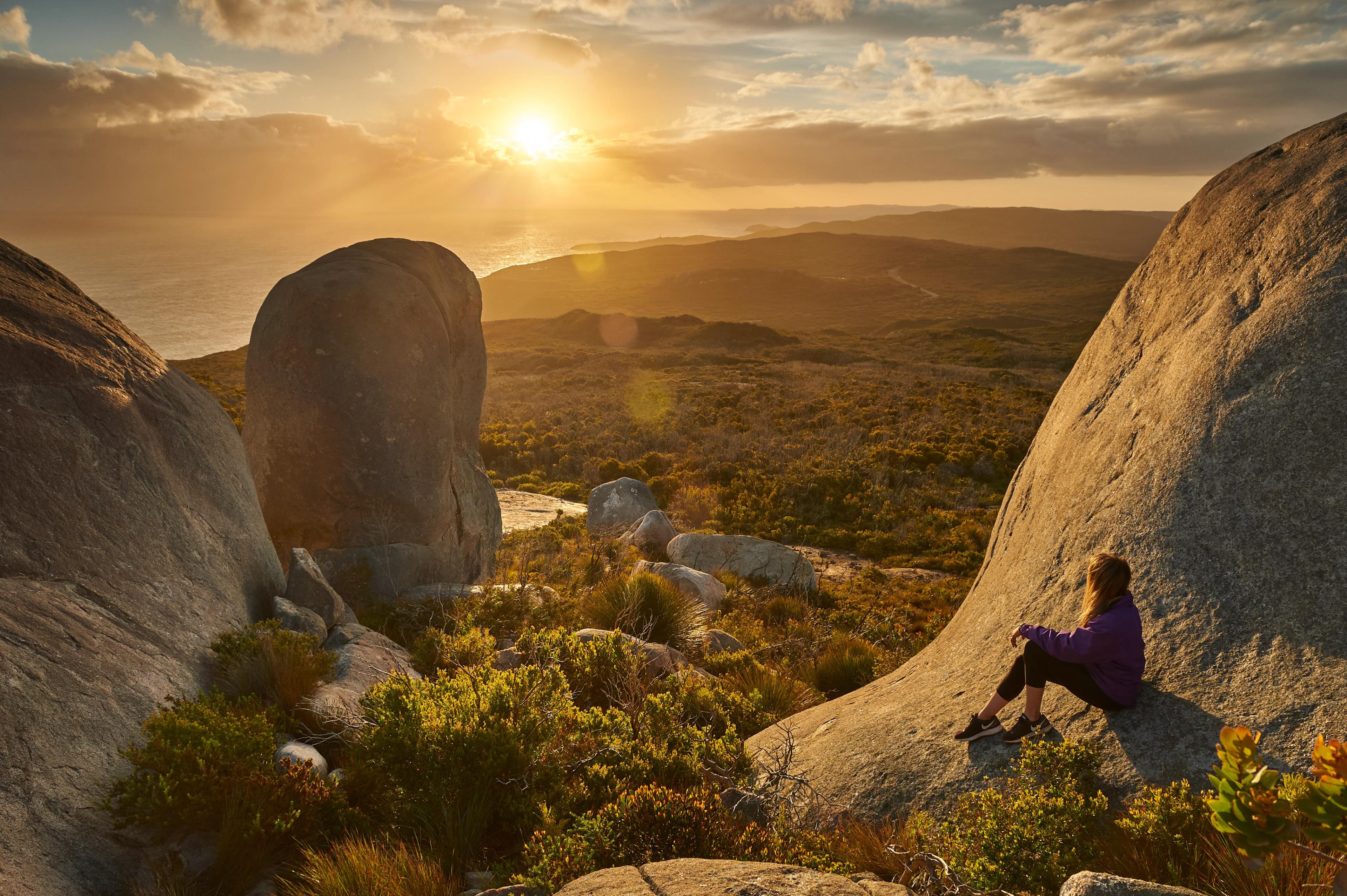 A woman sitting at Stony Hill watches the sunset from the Torndirrup peninsula