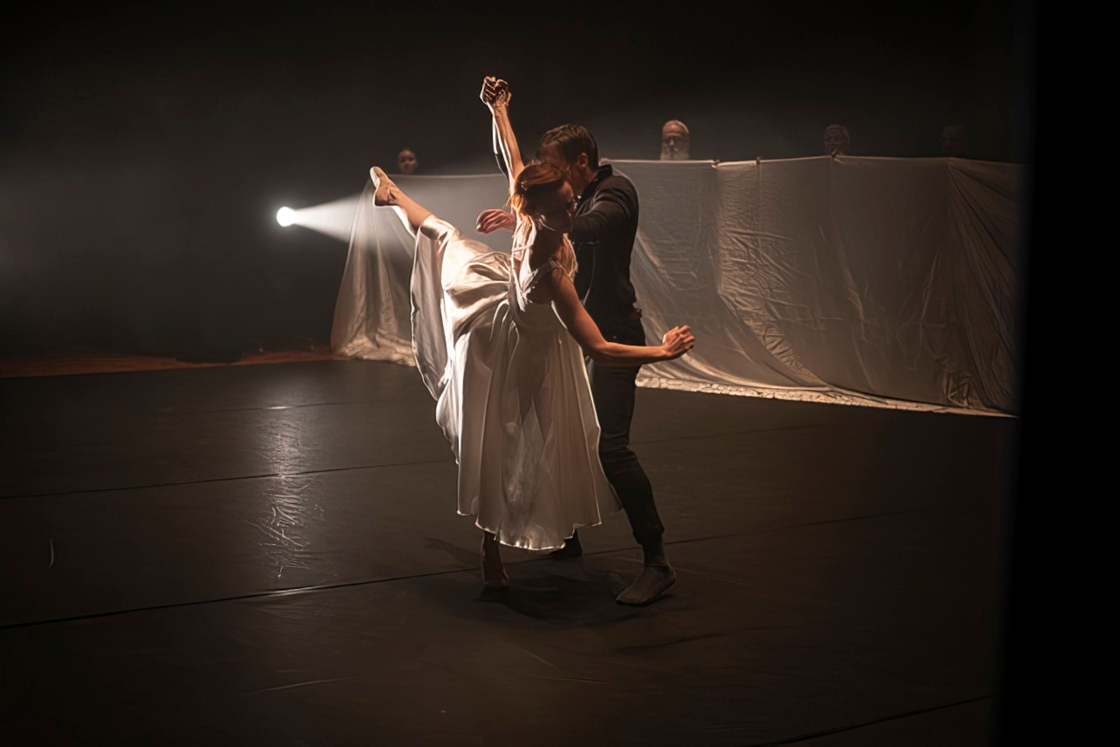 A male and female dancer, mid-pose, illuminated before a dark background