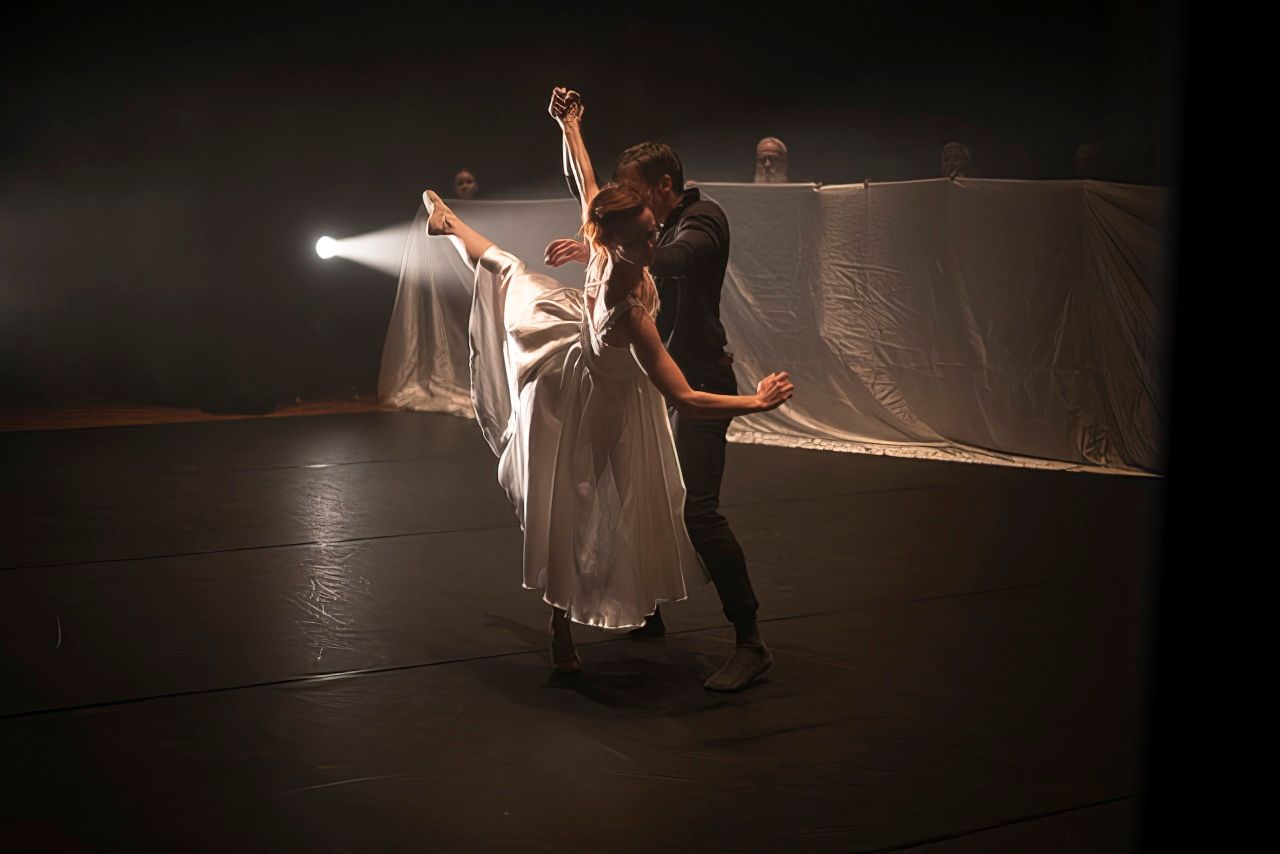 A male and female dancer, mid-pose, illuminated before a dark background