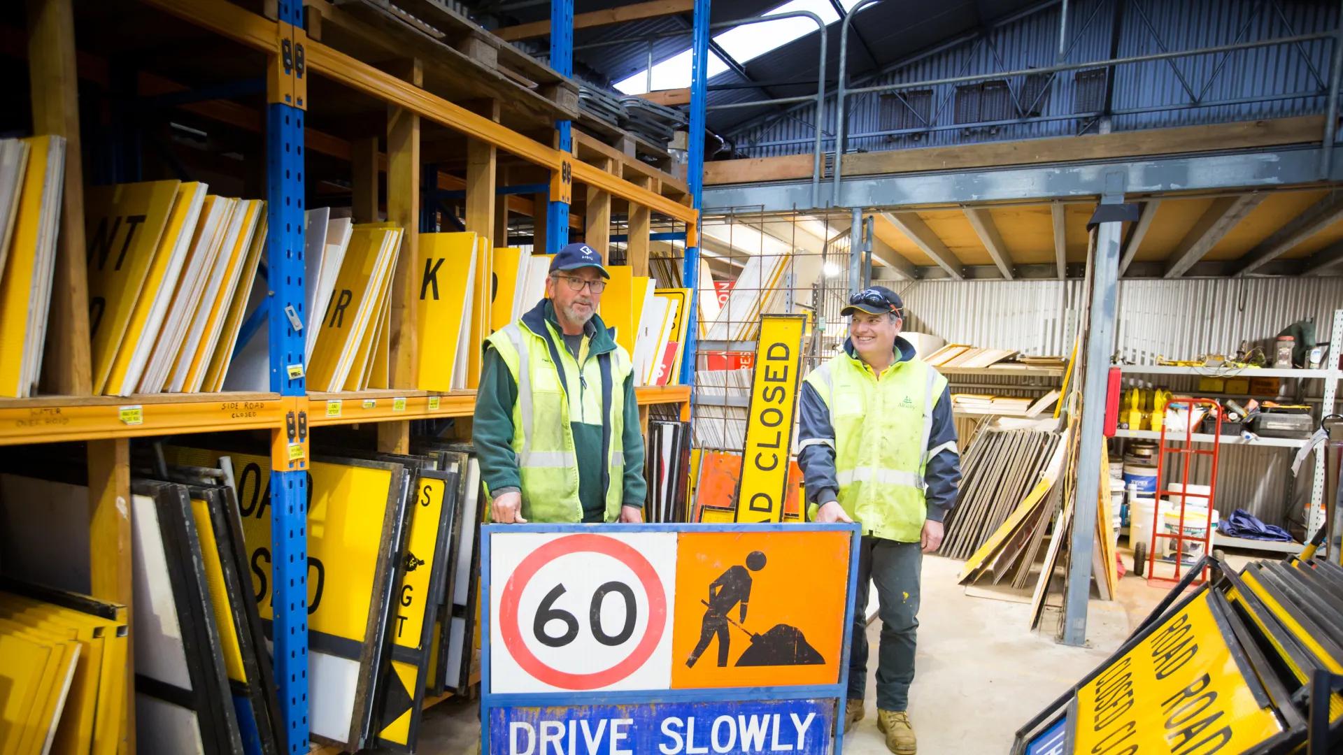 A photo of some workers standing in front of a drive slowly sign.