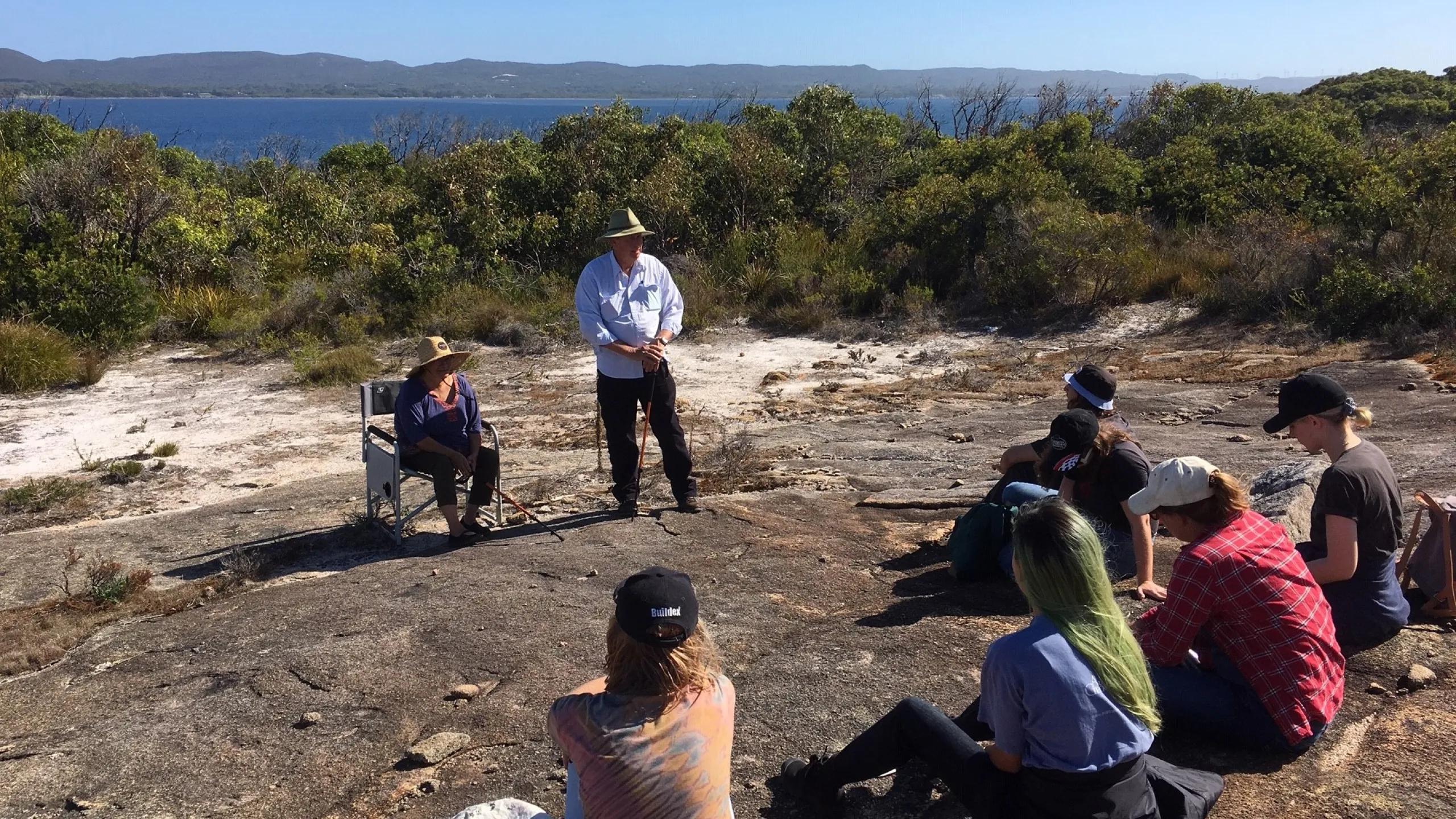 A photo of a group of people sitting on a rocky area in front of the ocean.