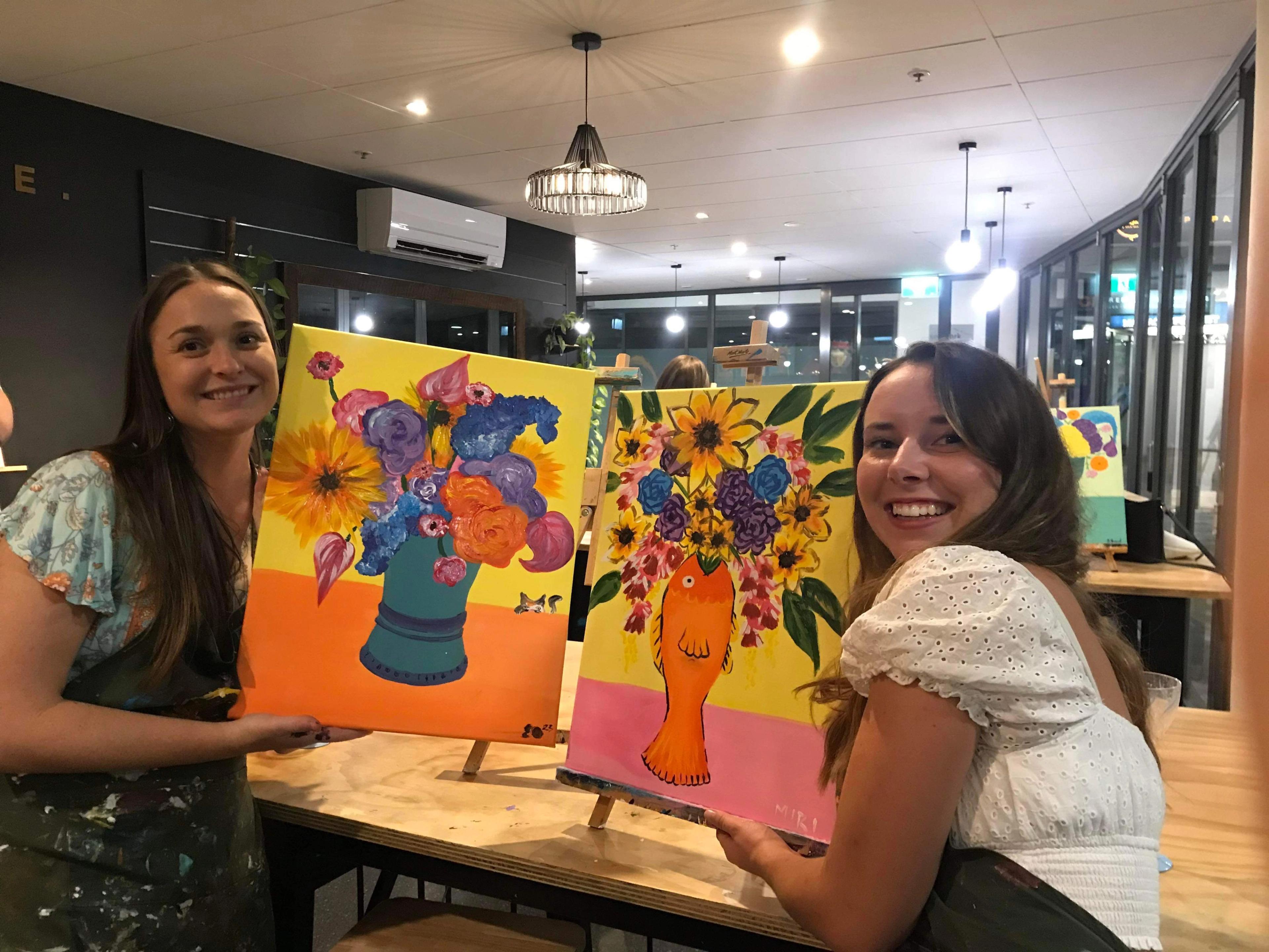 Two girls holding bright canvases of flowers