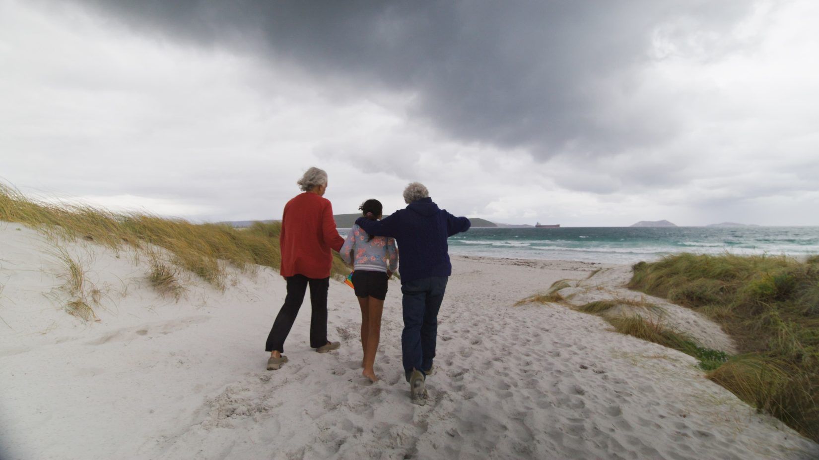 Three people walk out onto a beach in overcast weather