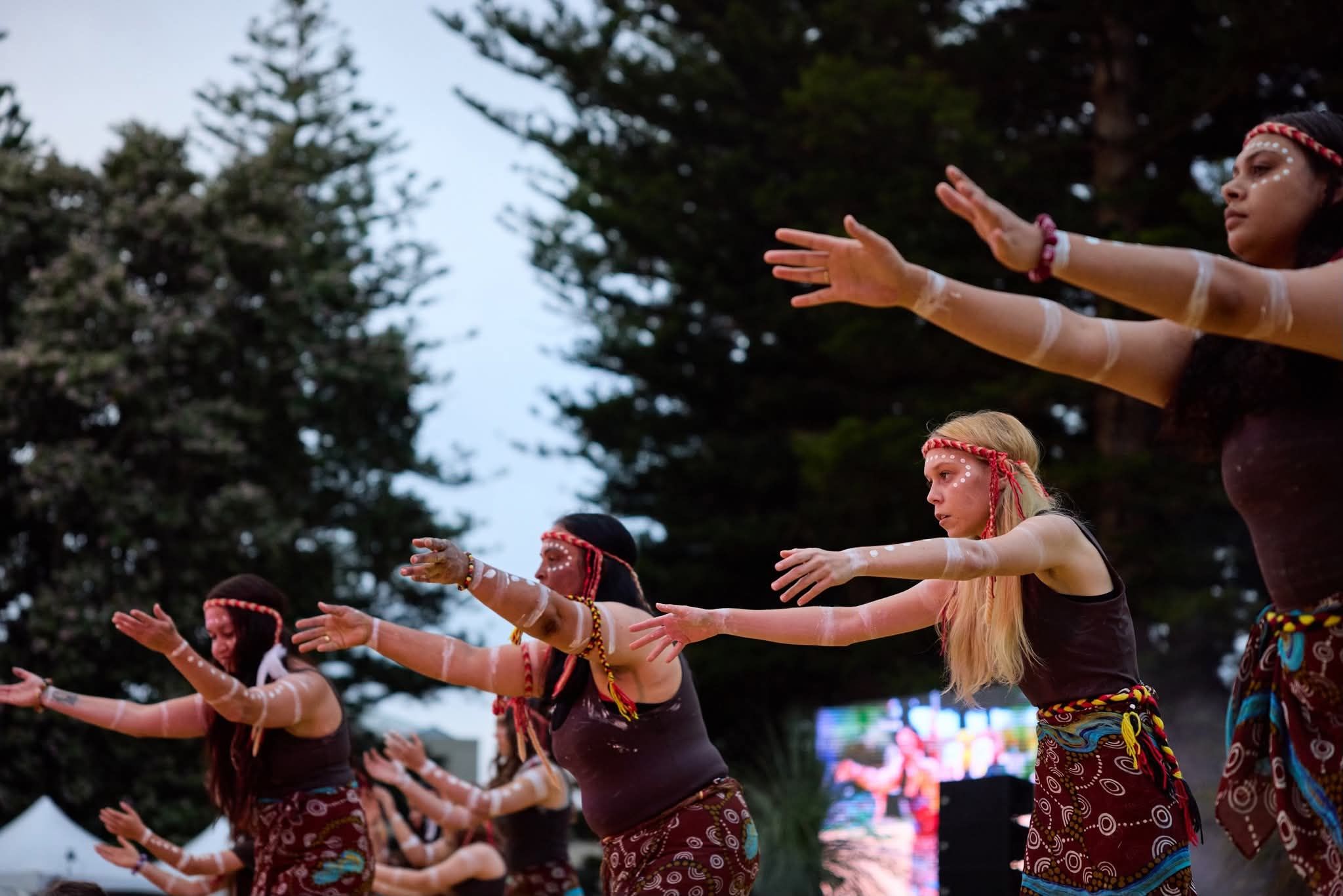 A group of young female Aboriginal dancers with arms raised