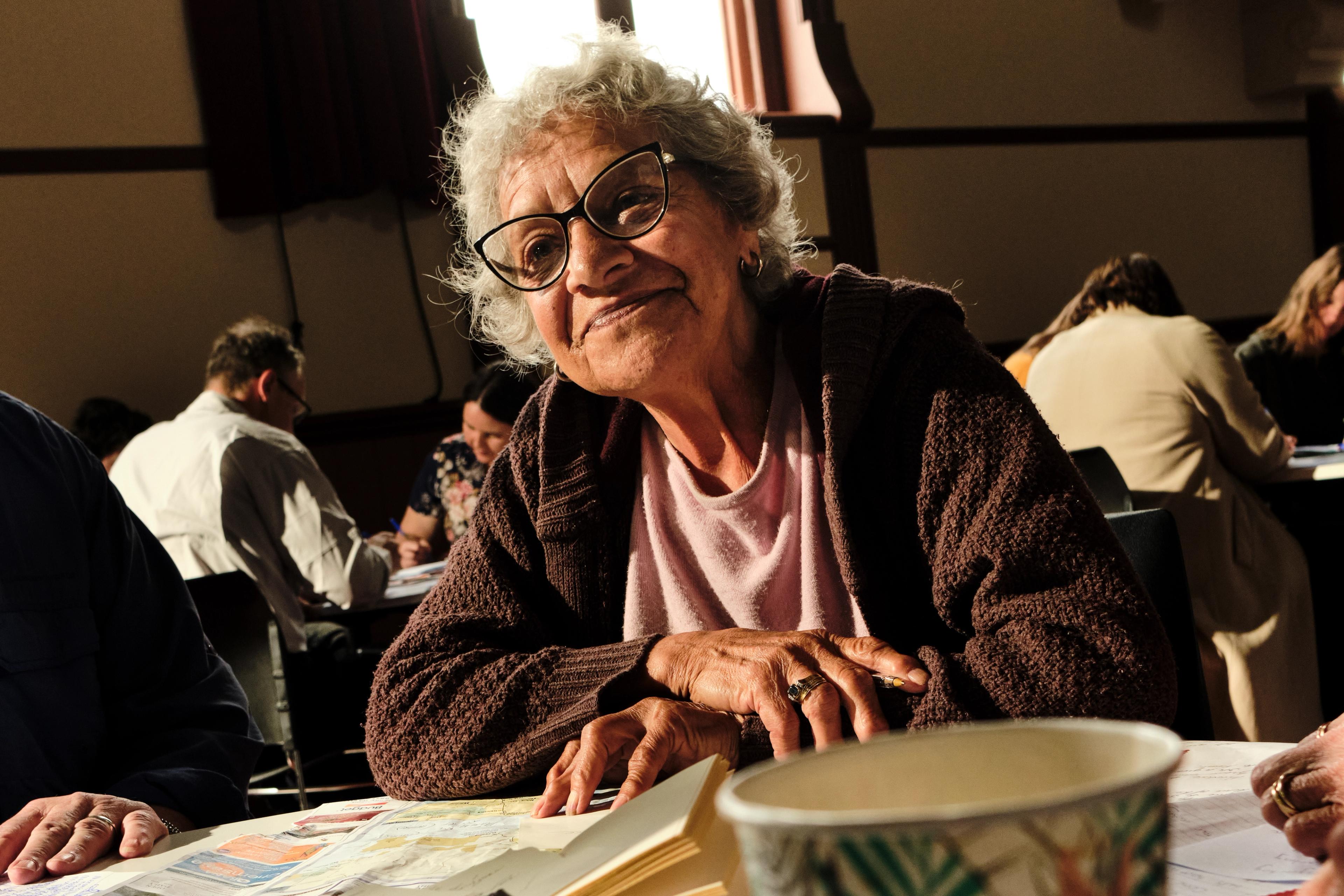 A photo of a women sitting down with arms folded and leaning in