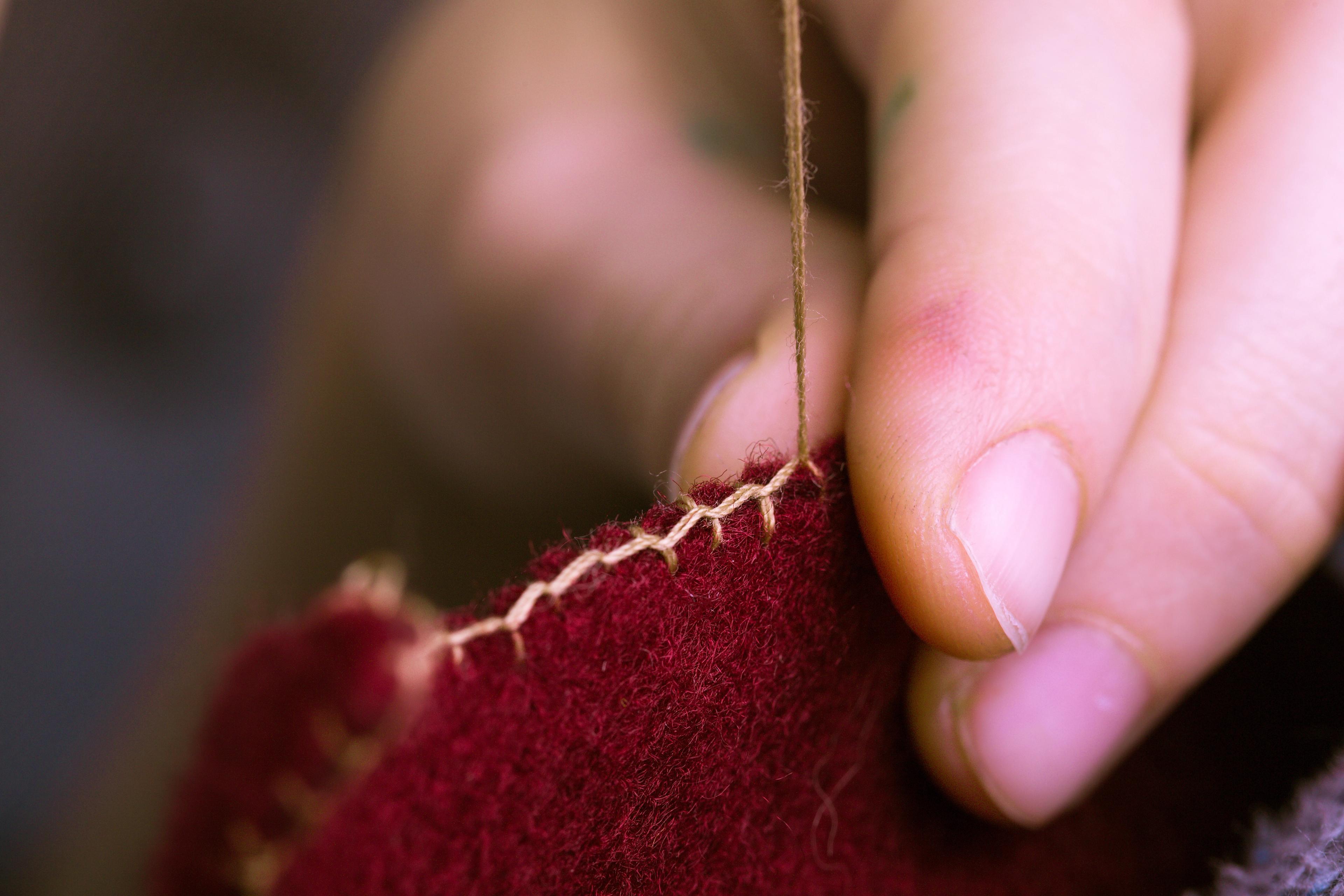 Image of a hand stitching some ruby red felt