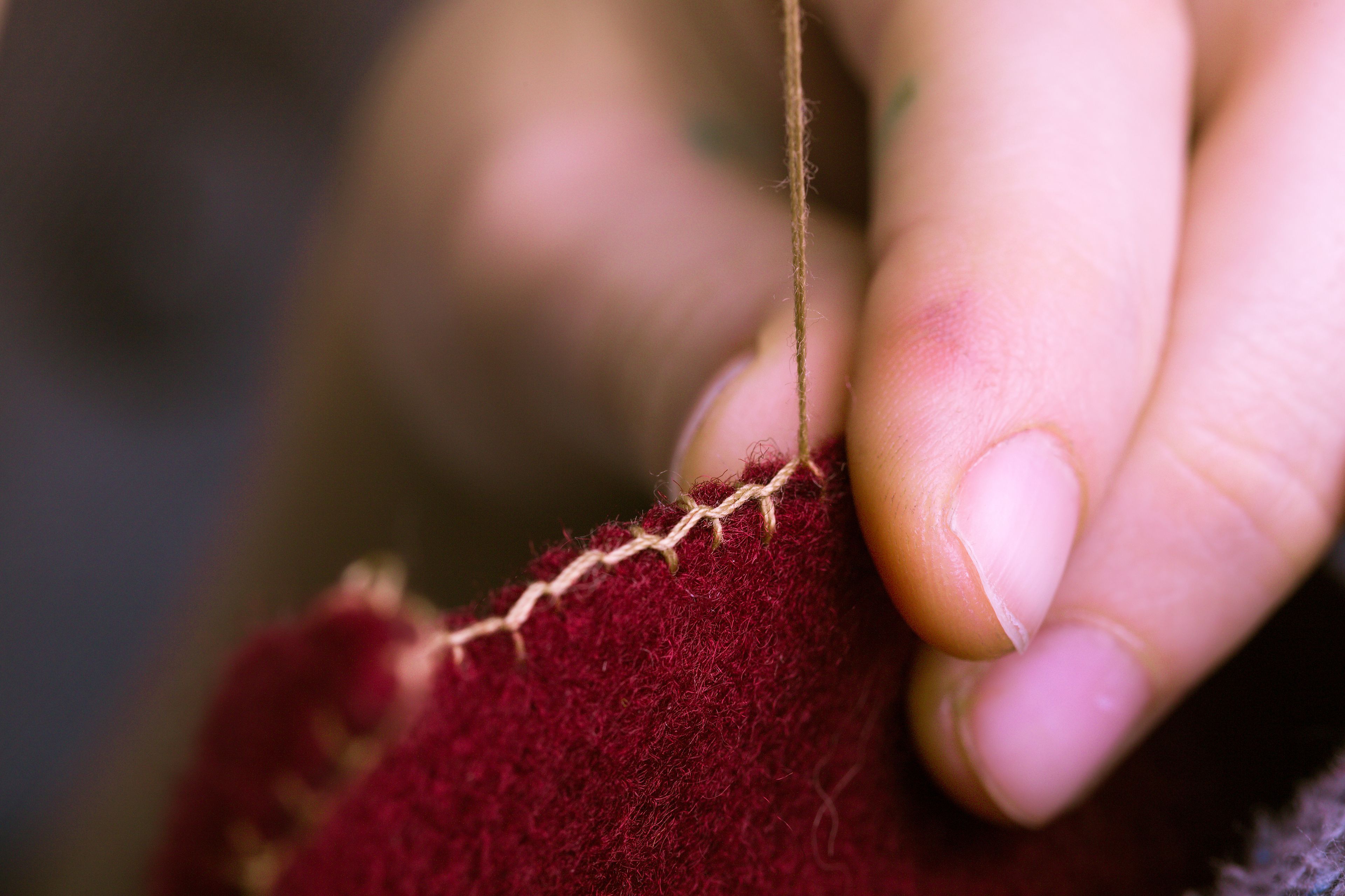 Image of a hand stitching some ruby red felt