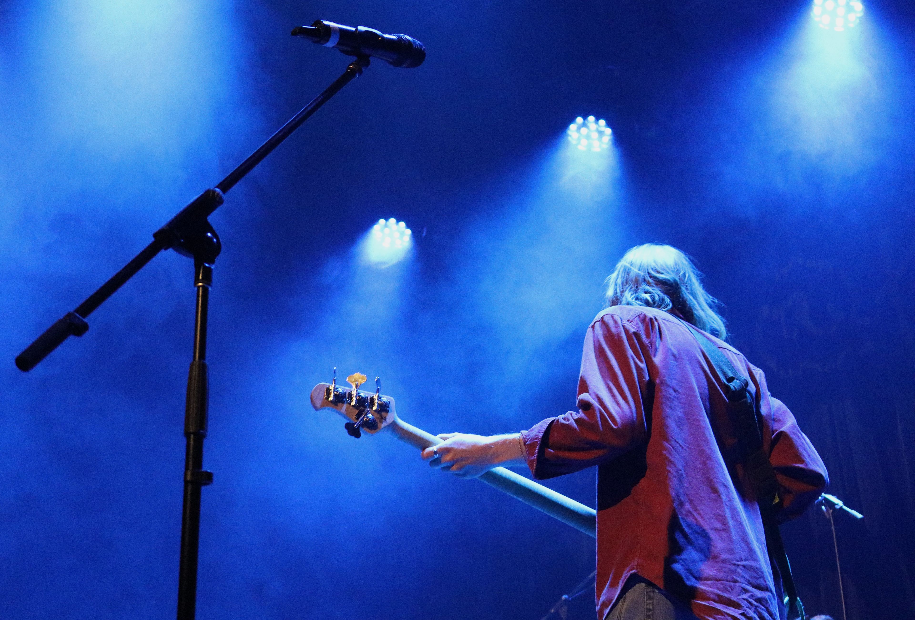 Man facing away holding a guitar under blue stage lights