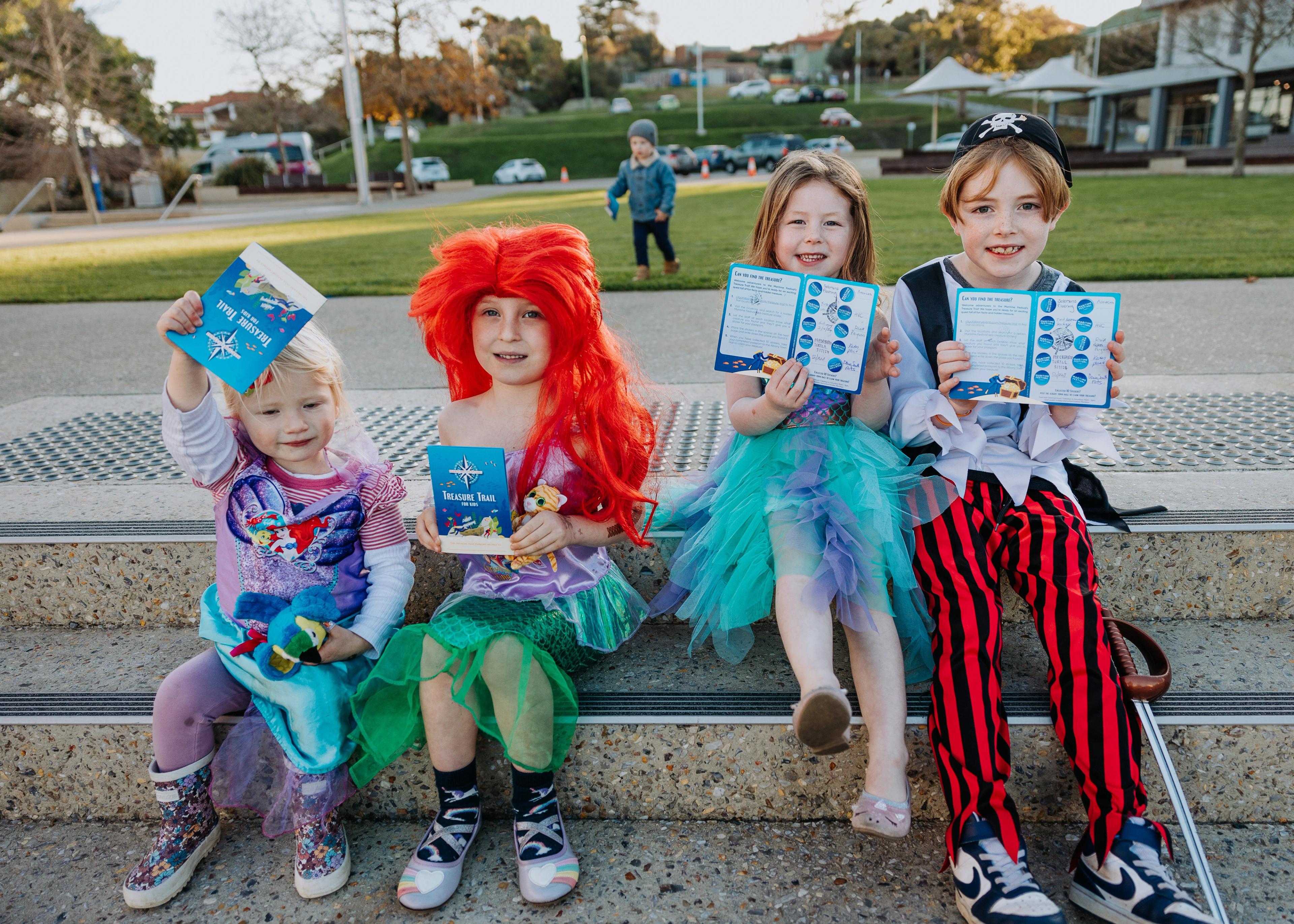 Four dressed-up children hold up their Treasure Trail passports