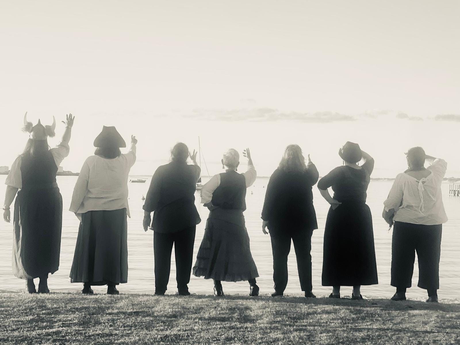 Image of the She Shants with their back to the camera, raising their arms out towards the sea.