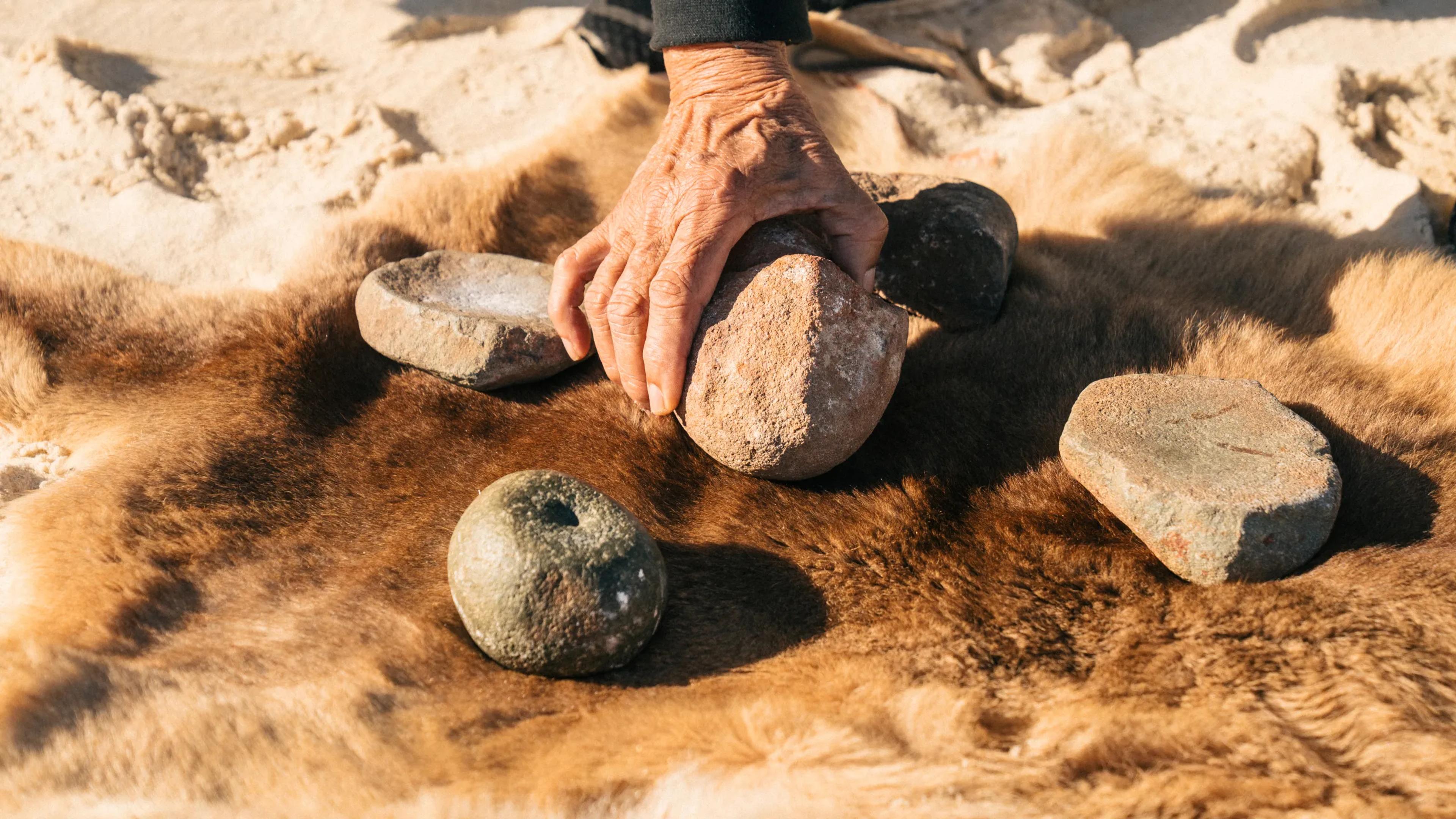 A photo of a hand coming in from the top of the frame, picking up a stone.