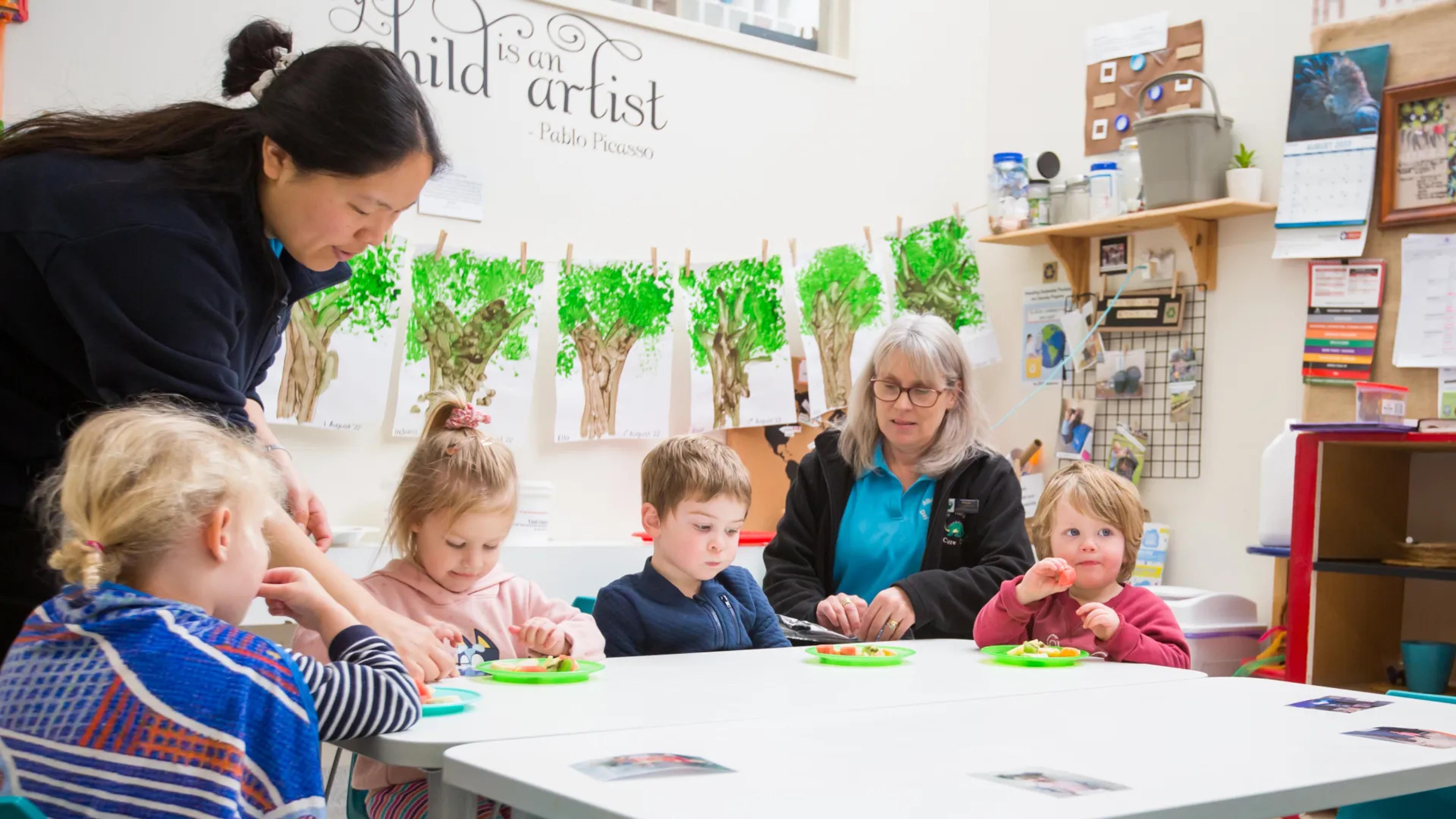 A photo of a teacher and some children sitting at a desk doing an activity.