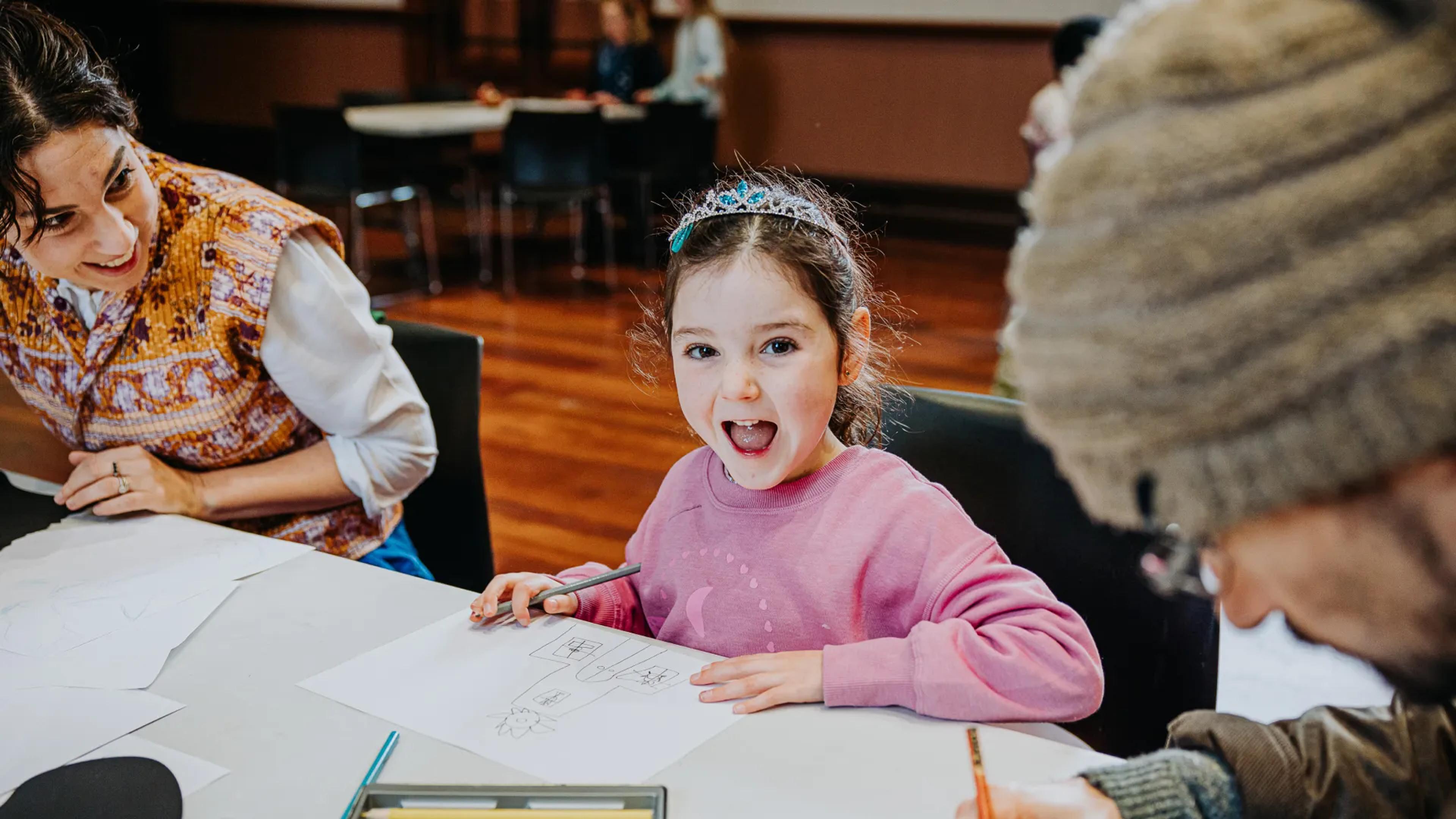 A photo of a girl sitting at a table, drawing.