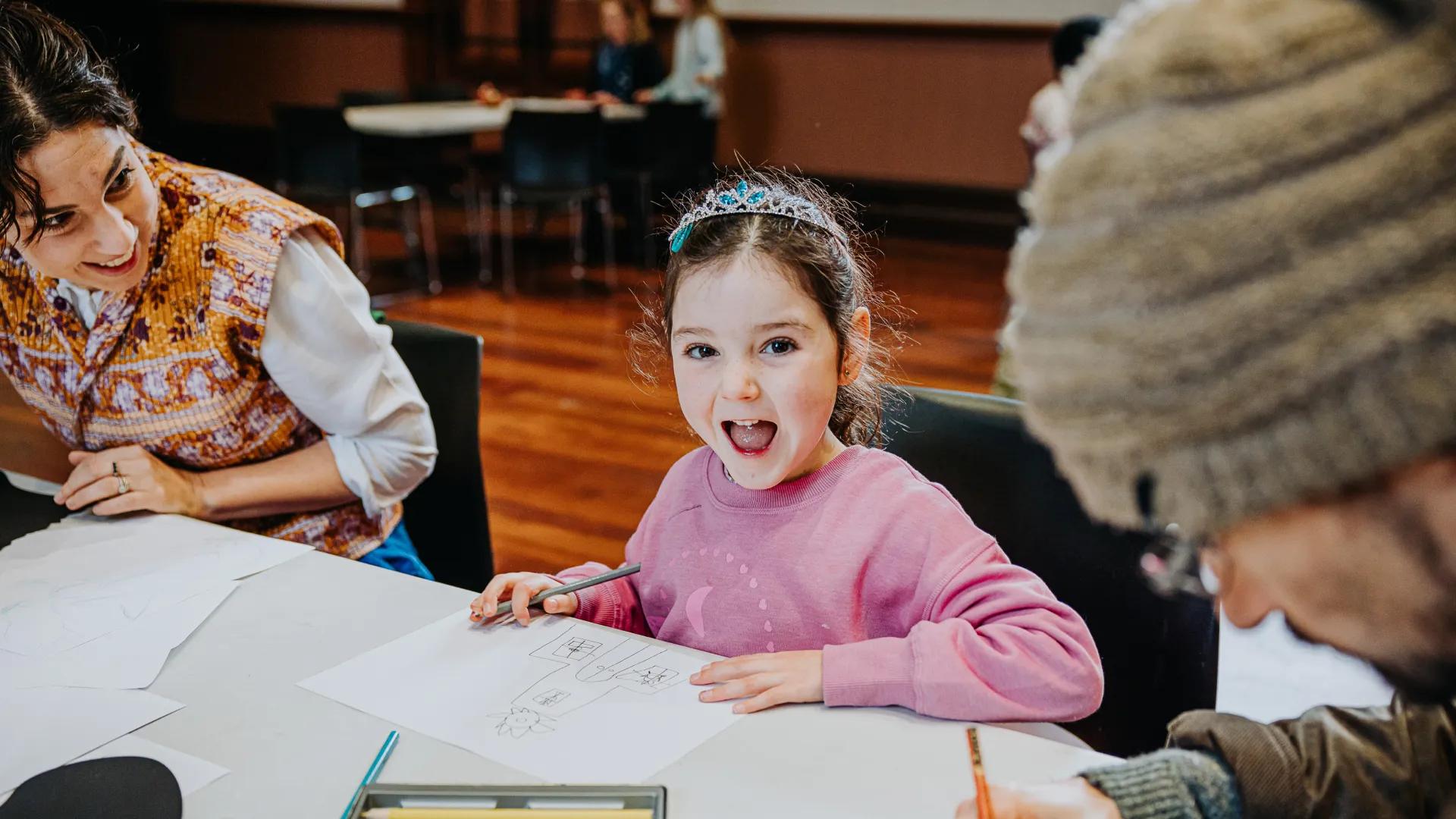 A photo of a girl sitting at a table, drawing.