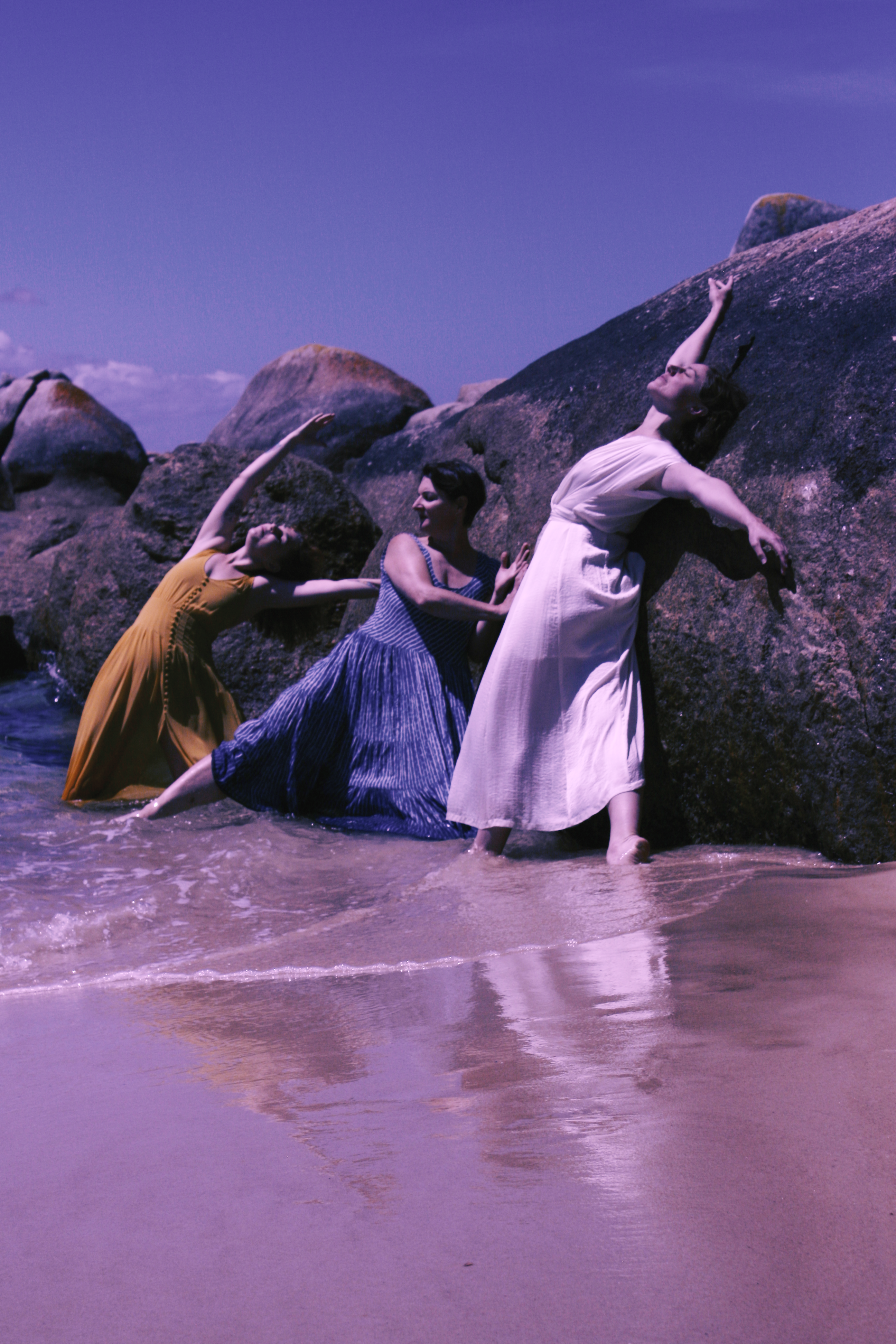 Three women dancing in the ocean next to rocks