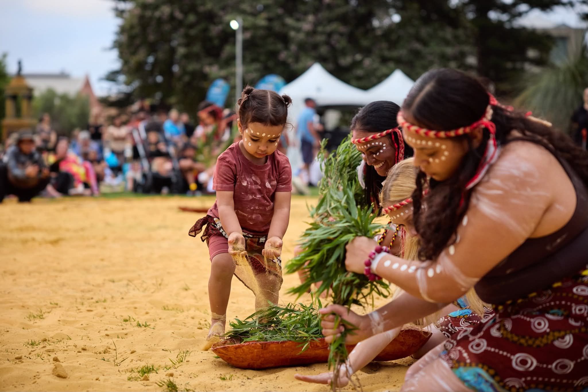 Toddler girl and Aboriginal female dancers seated with leaves
