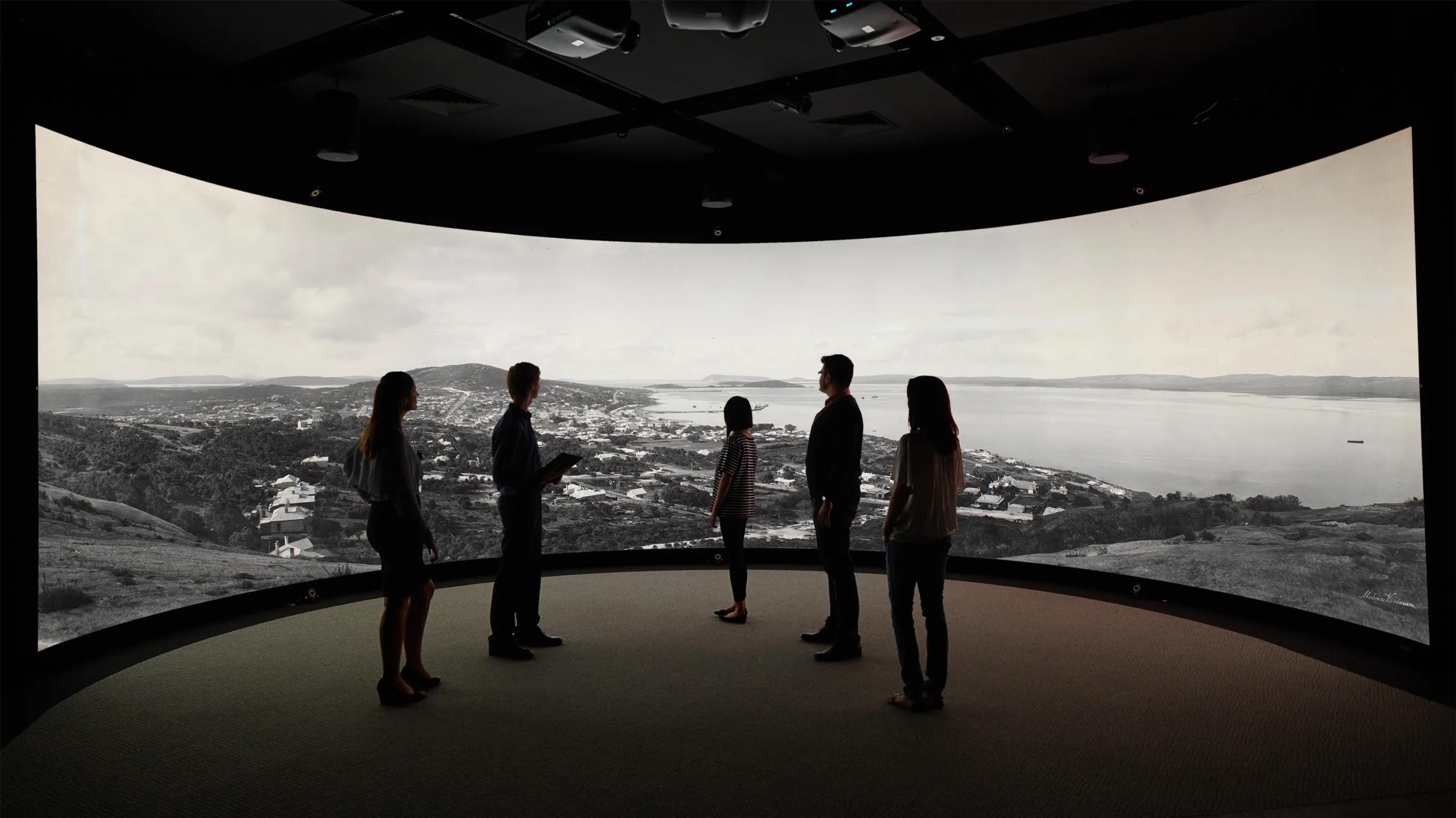 A photo of 5 people standing in front of a screen showing Albany on it.