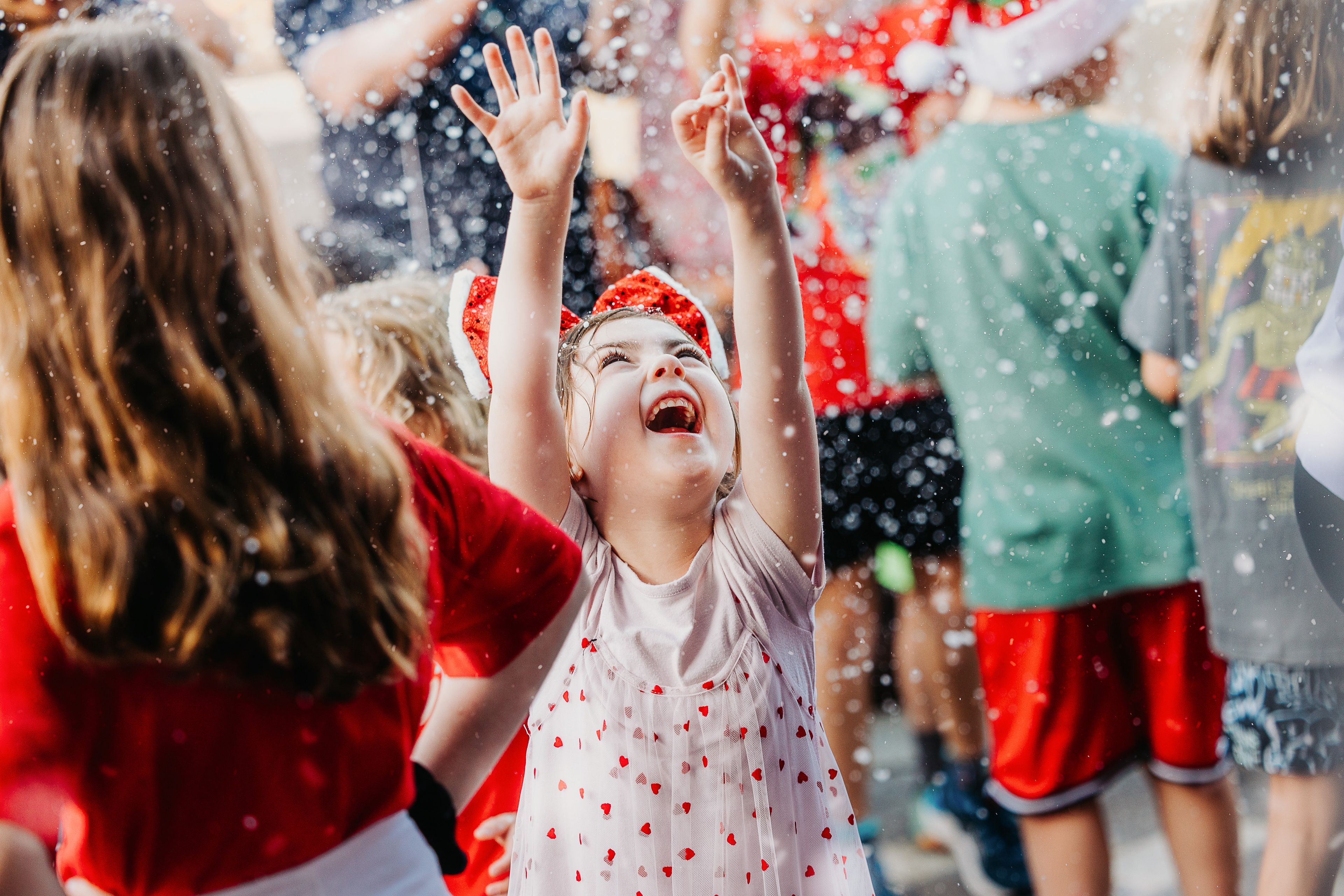 A little girl stretches her arms up towards falling snow