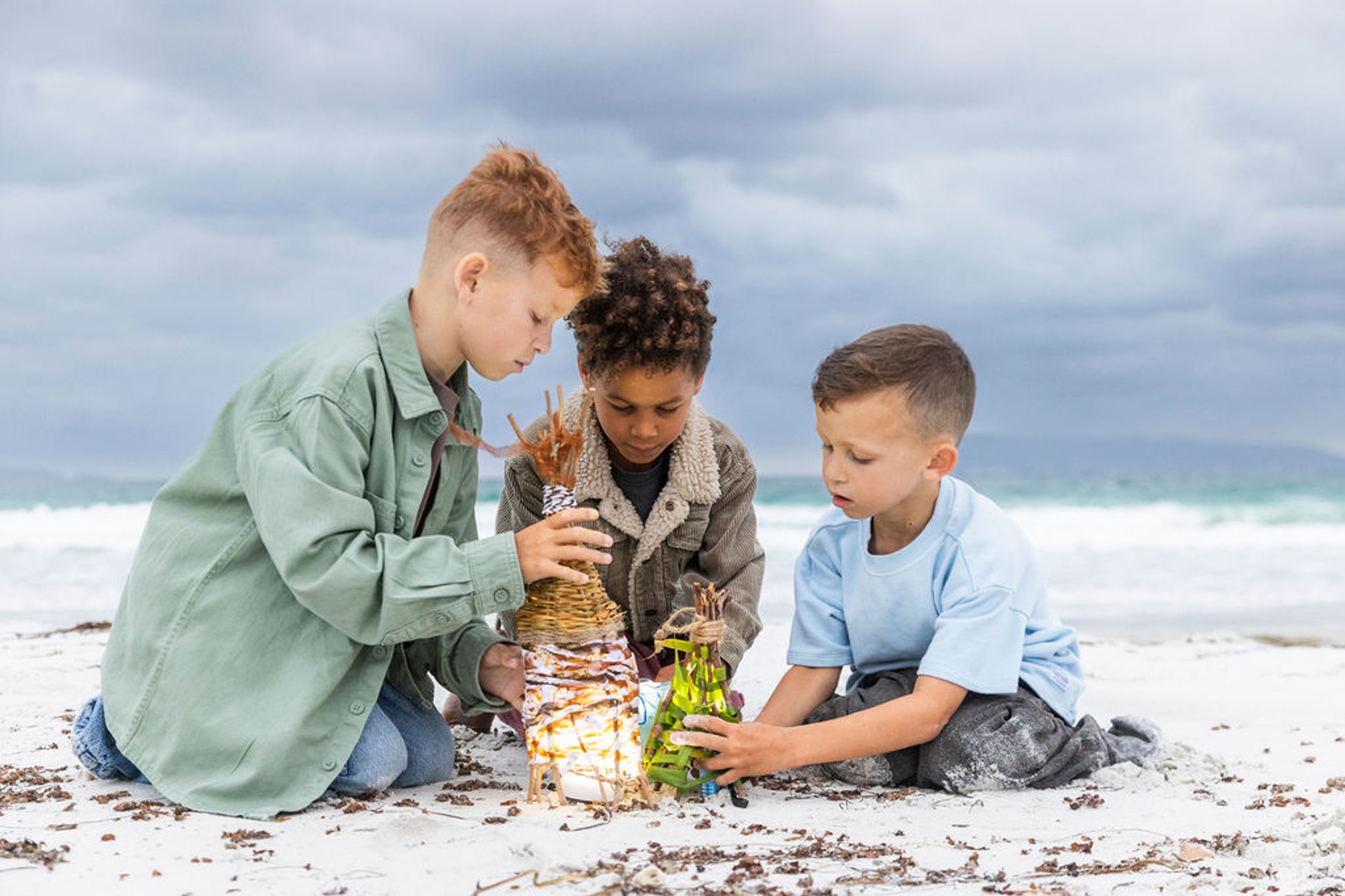 Three young boys on a beach with homemade lanterns
