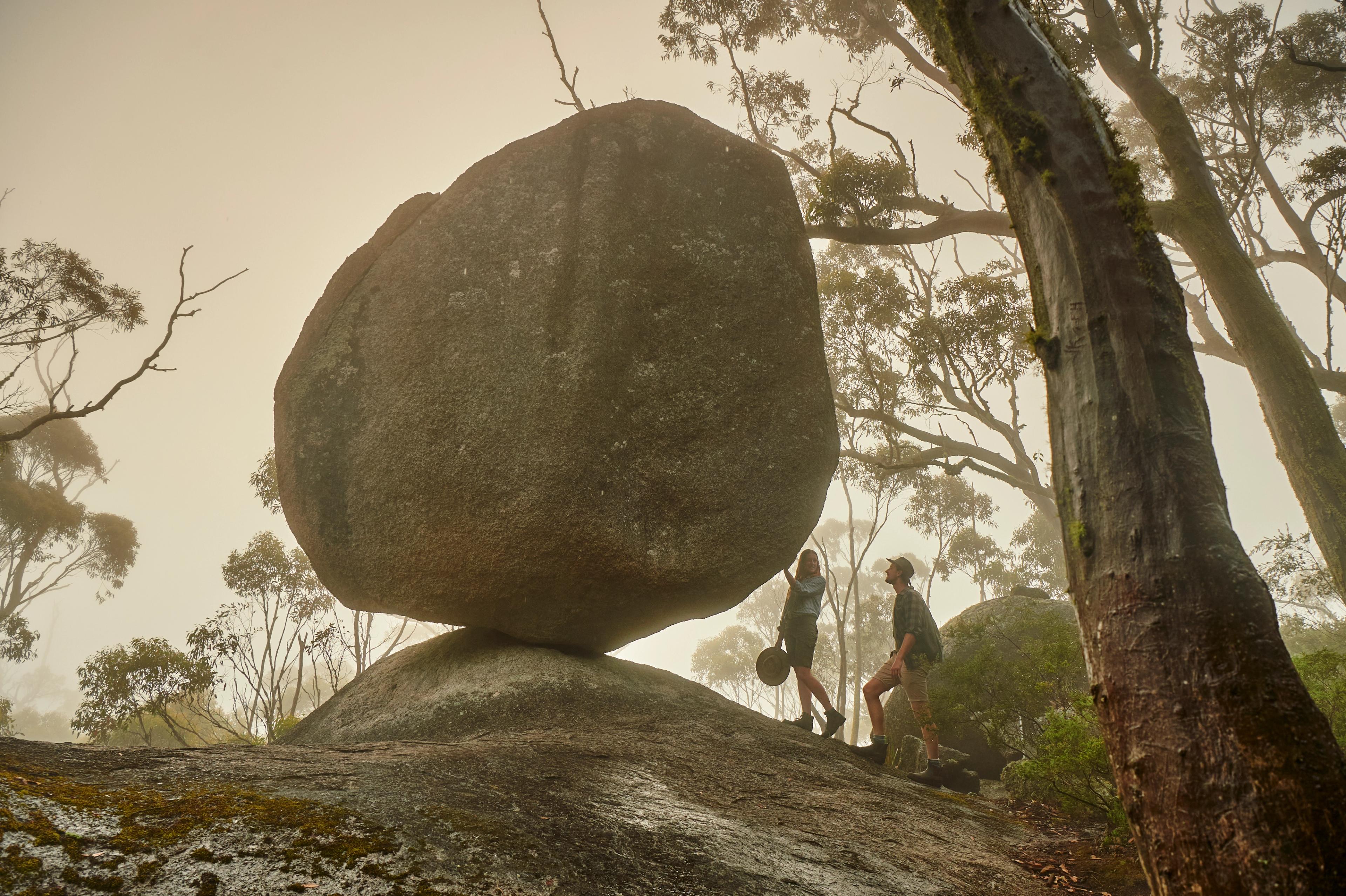 Two people on a hike admiring a huge granite stone that is balancing on its edge