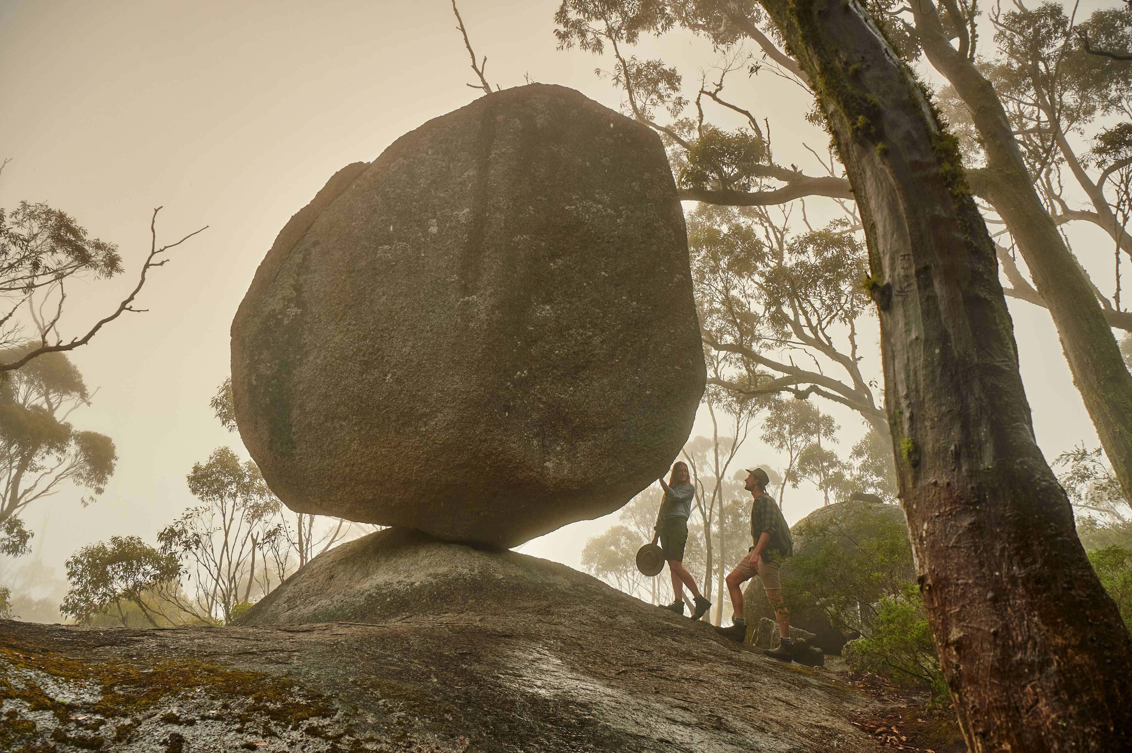 Two people on a hike admiring a huge granite stone that is balancing on its edge