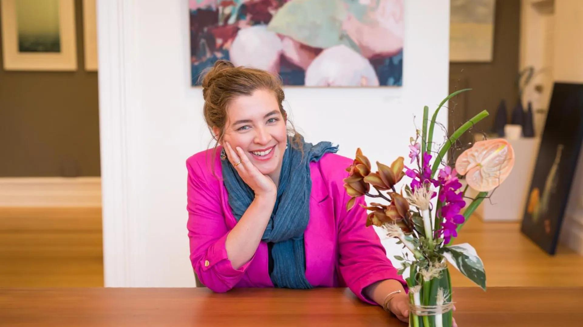 A photo of a woman sitting at a table with some flowers in front of her.