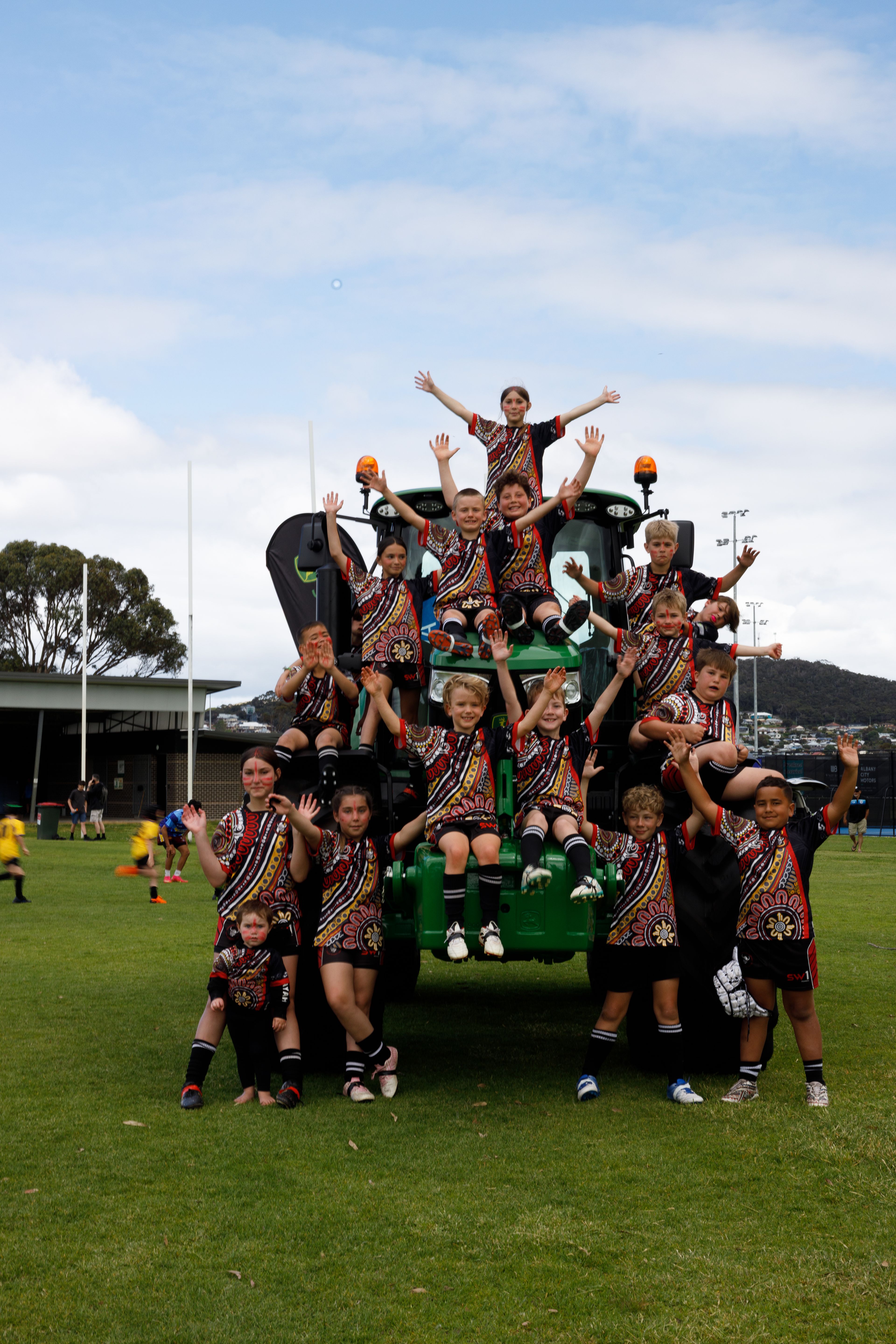 A large group of children pose in front of a tractor on the rugby field. 