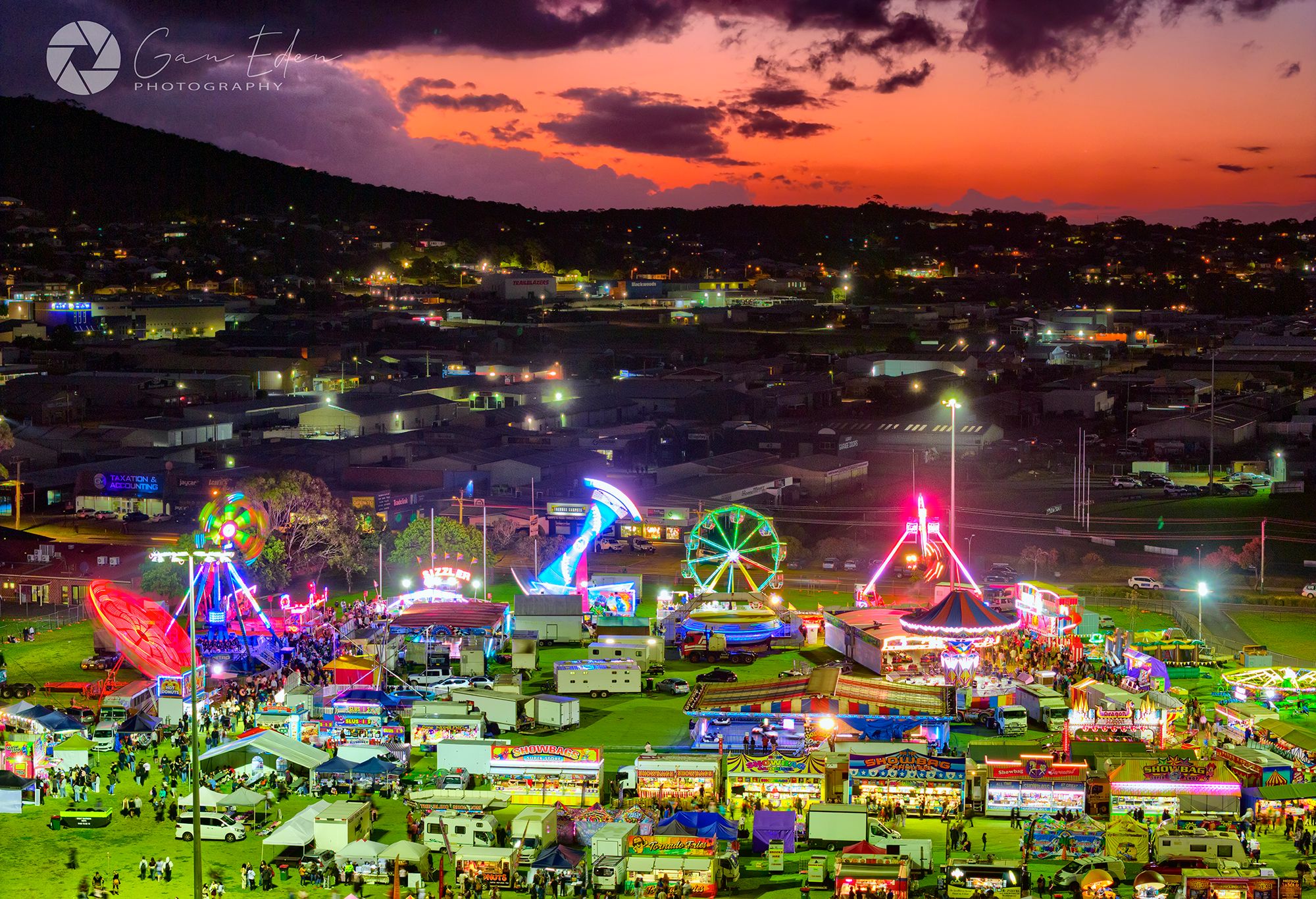 Aerial image of a show ground, with the rides illuminated against a peach-coloured sunset.
