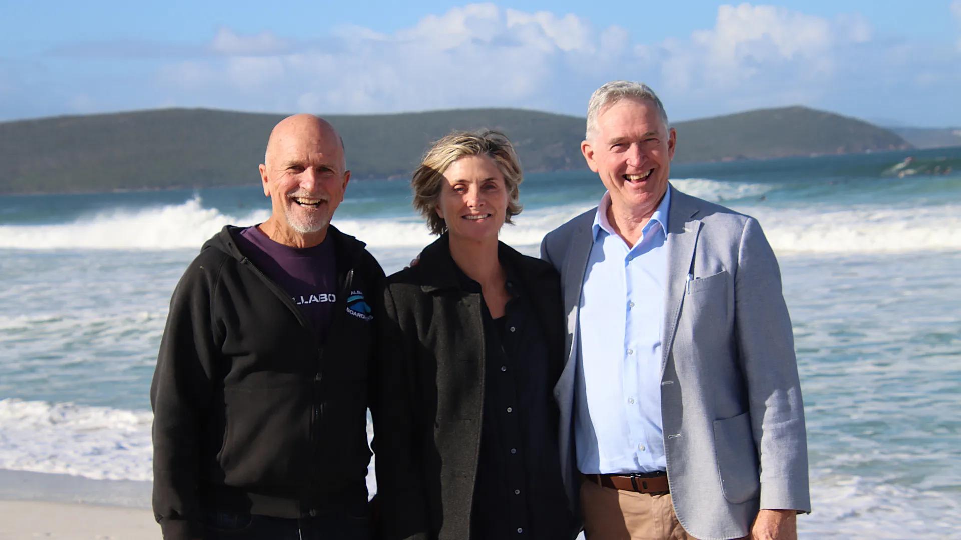 A photo of two men and a woman standing in front of the beach.