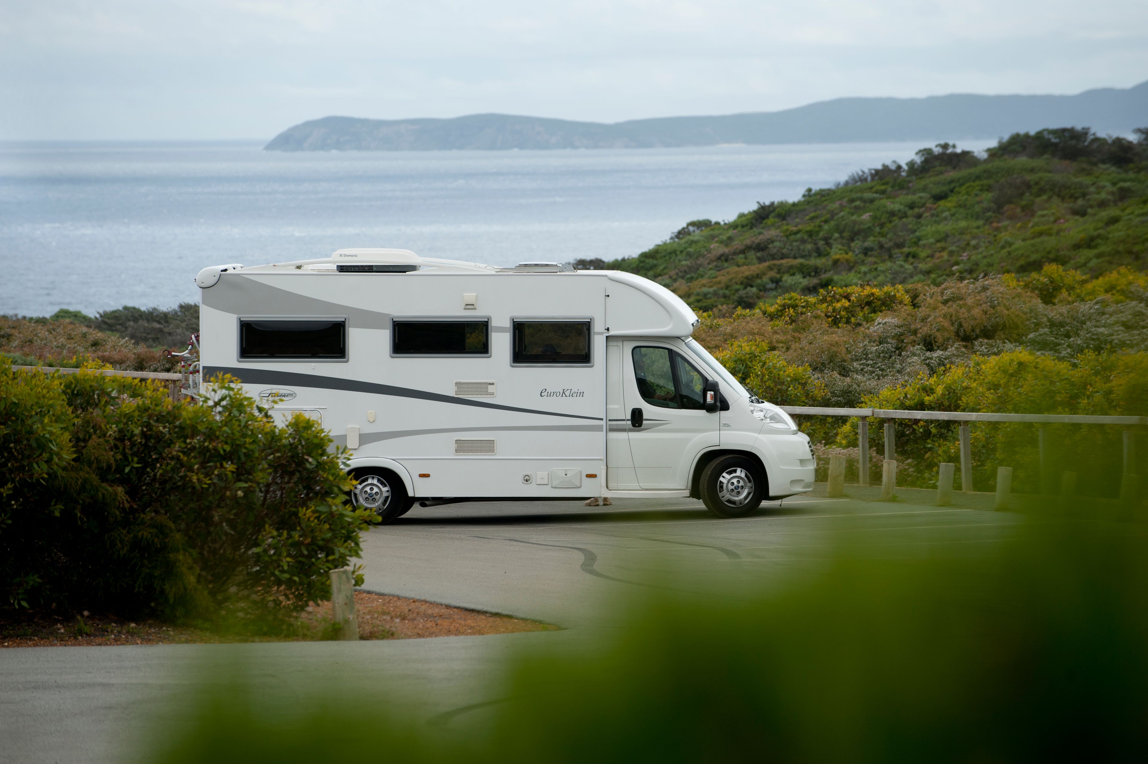 A RV parked amongst the bush with ocean views in the background
